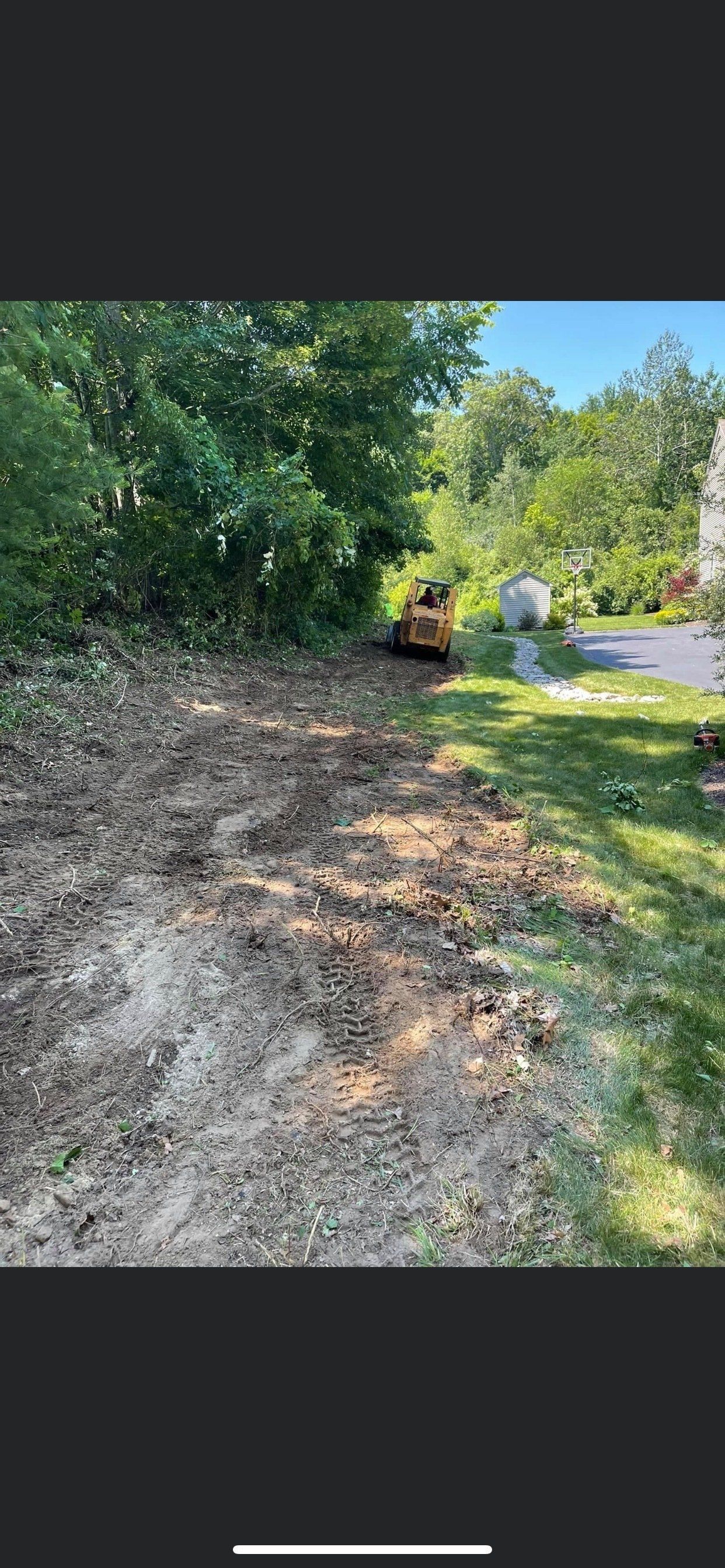 A dirt road surrounded by trees and grass with a bulldozer in the background.