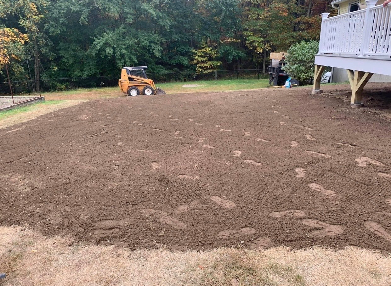 A bulldozer is moving dirt in a backyard next to a deck.
