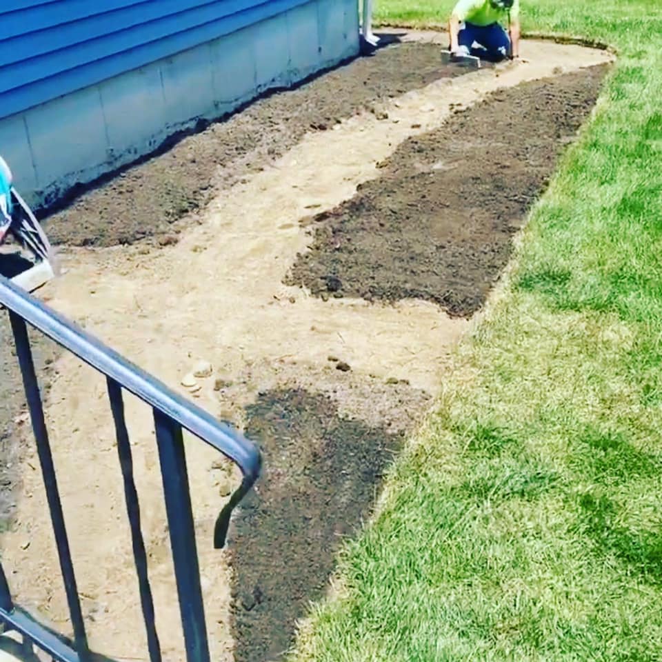 A man is working on a sidewalk in front of a house.