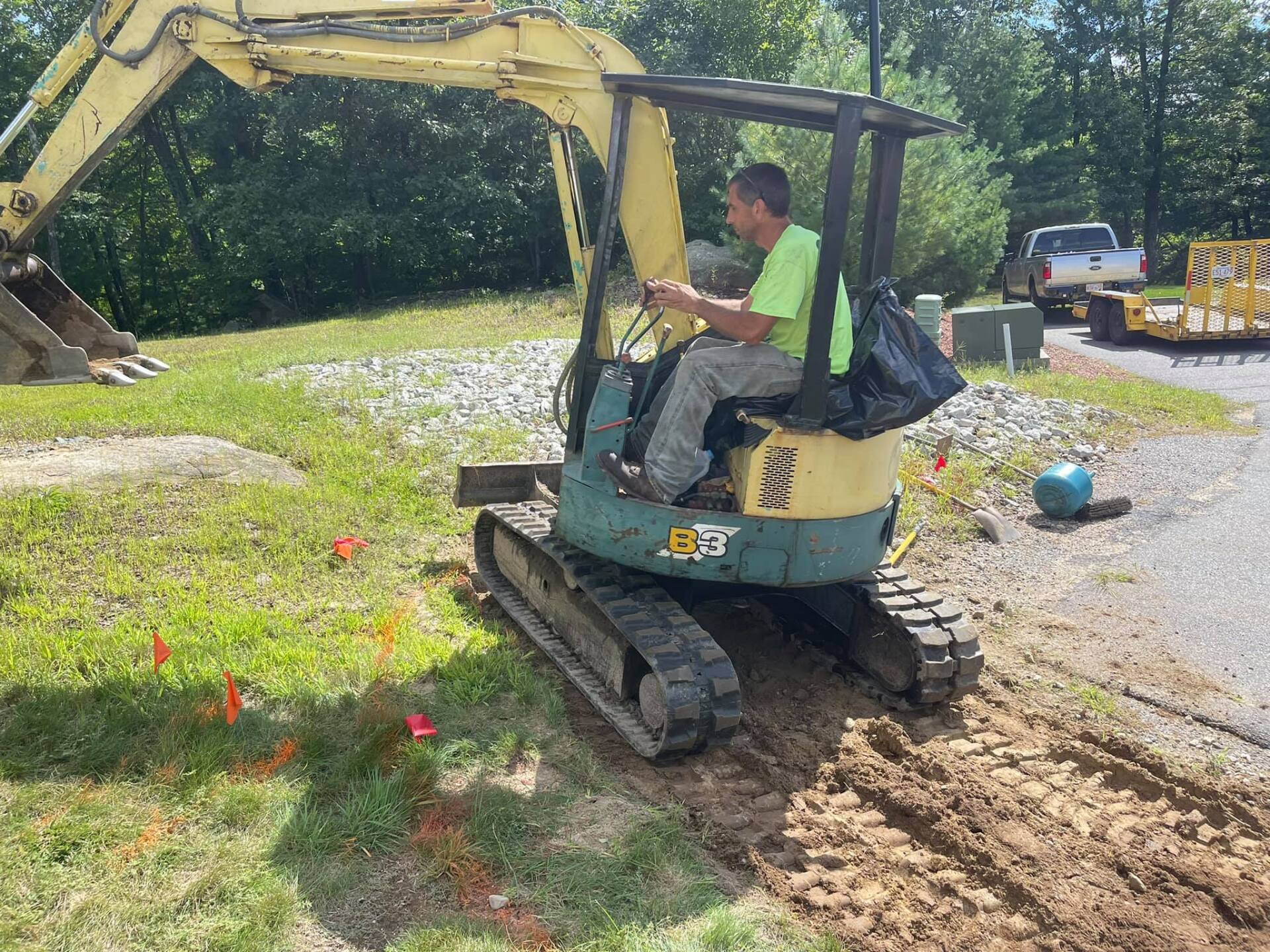 A man is driving a small excavator on a dirt road.