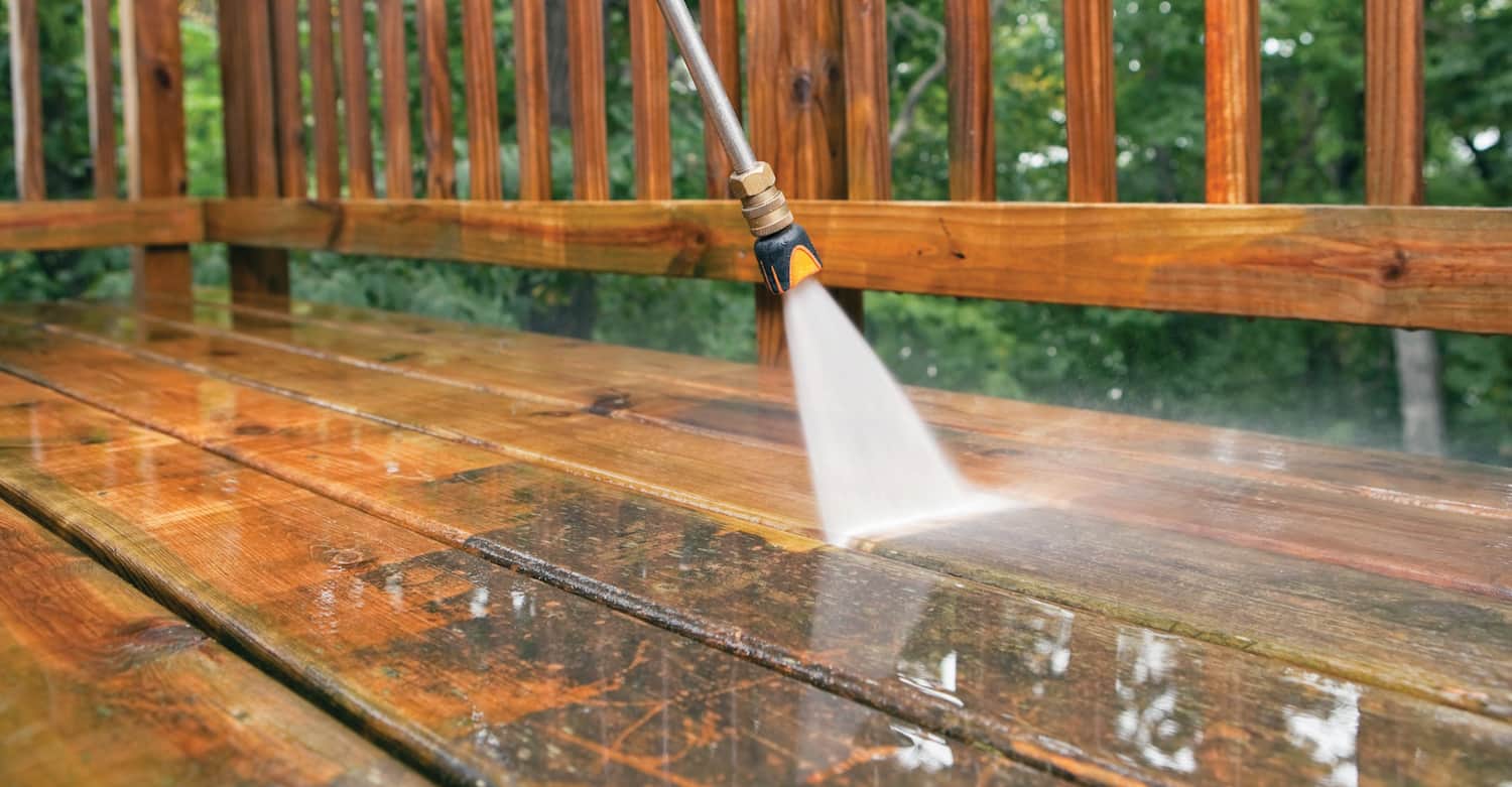 A person is using a high pressure washer to clean a wooden deck.