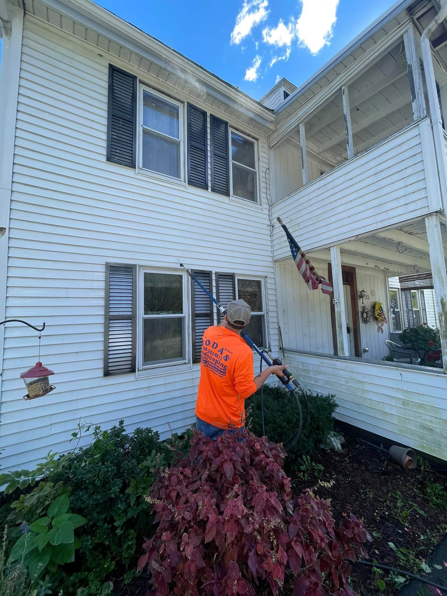 A man is cleaning the side of a white house with a pressure washer.