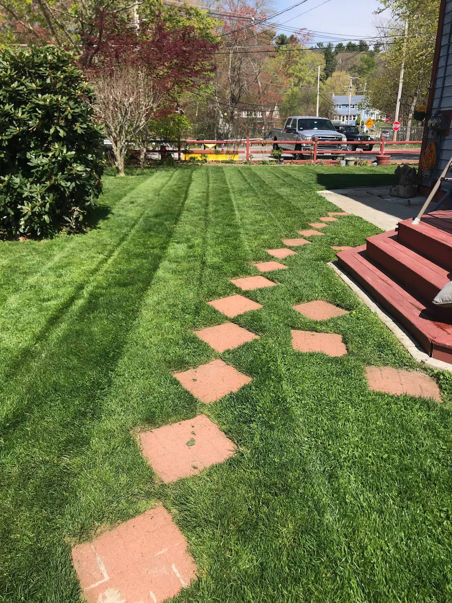 A lush green lawn with a brick walkway leading to a house.