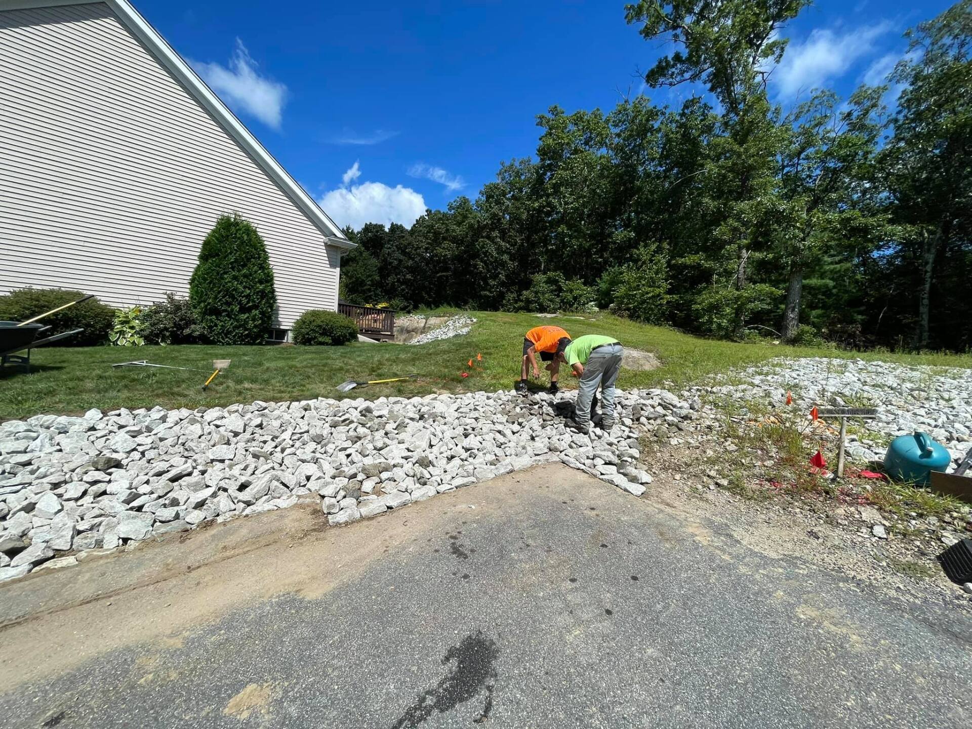 Two men are working on a gravel driveway in front of a house.