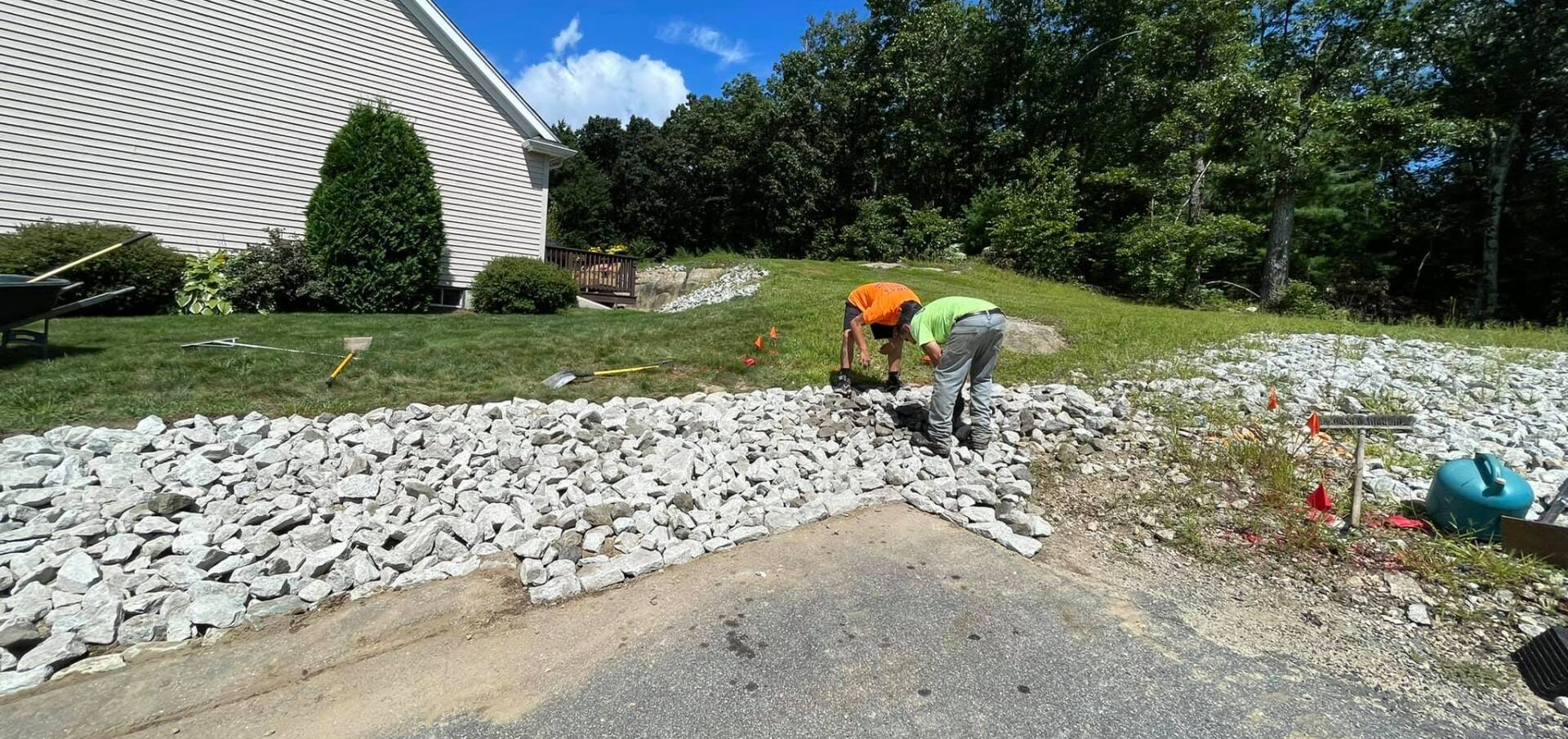 Two men are working on a gravel driveway in front of a house.