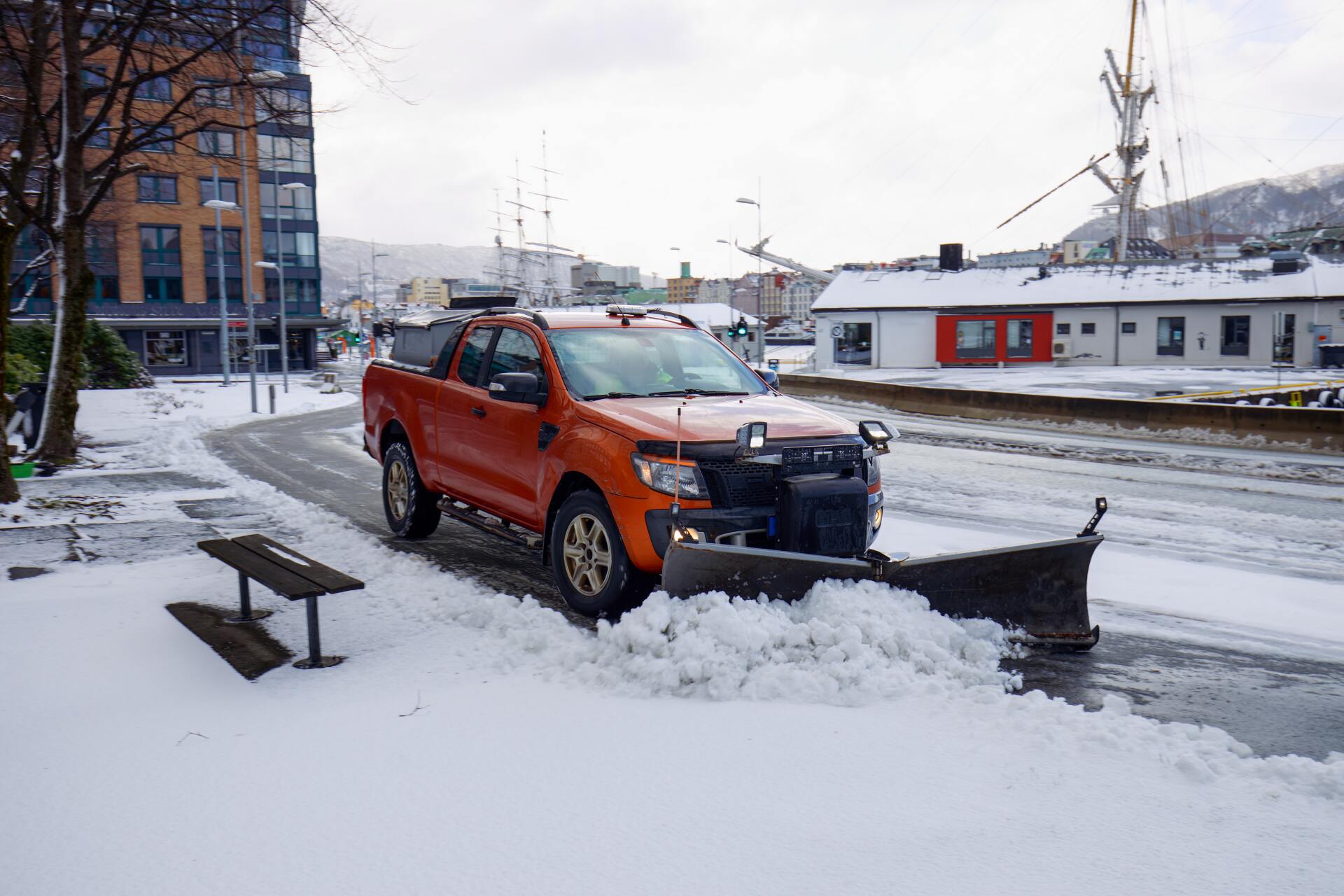 An orange truck with a snow plow on the front is plowing snow.