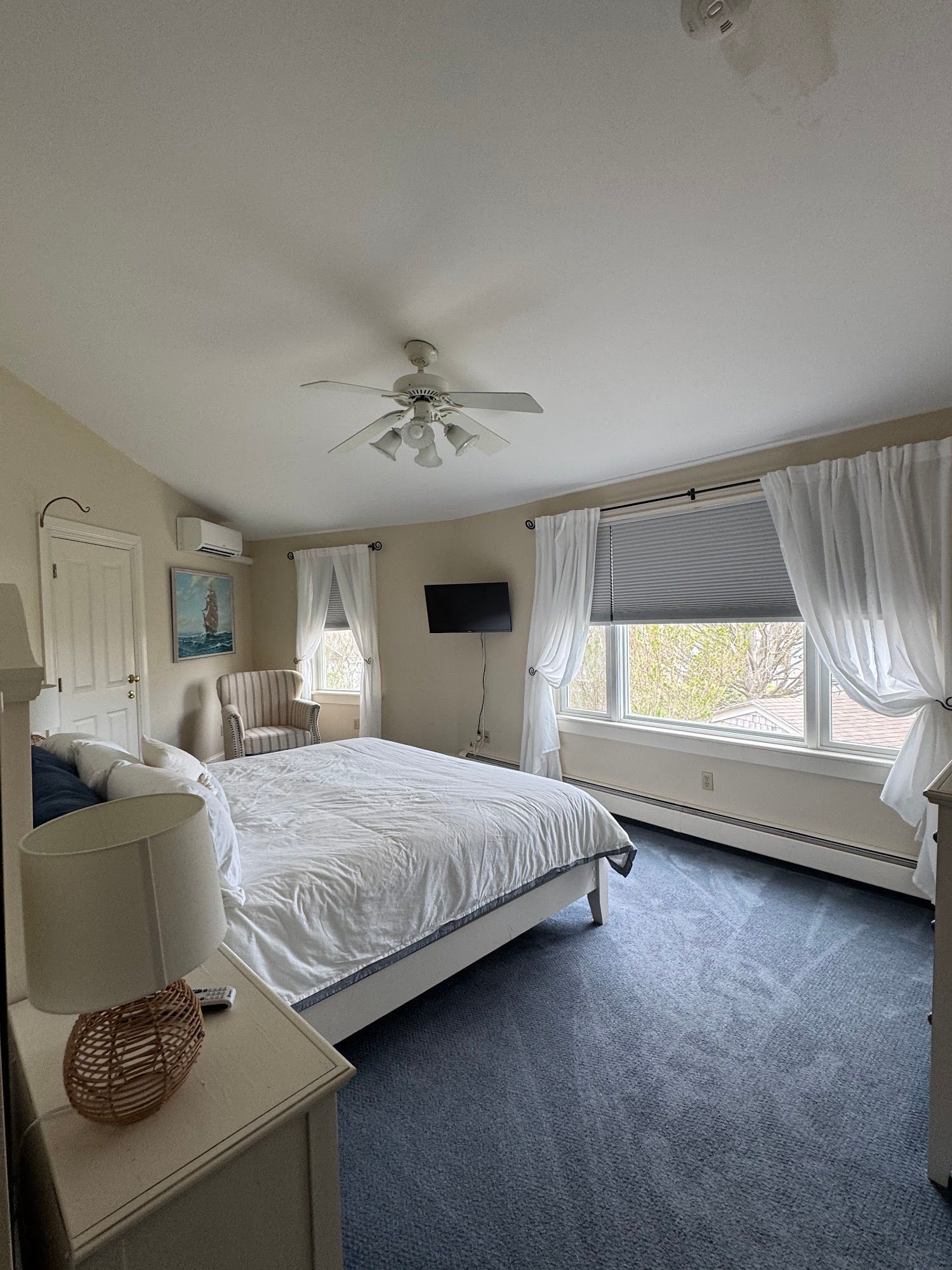 A bedroom with a king size bed , a ceiling fan , a chair and a television.