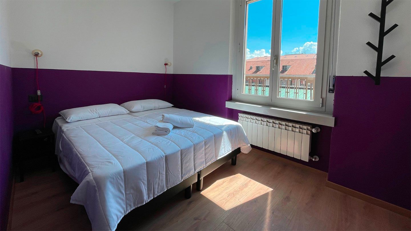 Bedroom with double bed, purple wall accents, white bedding, and sunny window.