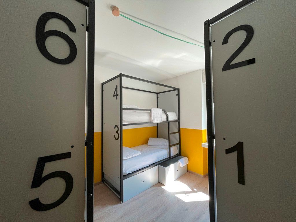 A room with bunk beds, viewed through numbered room dividers. Yellow and white walls.
