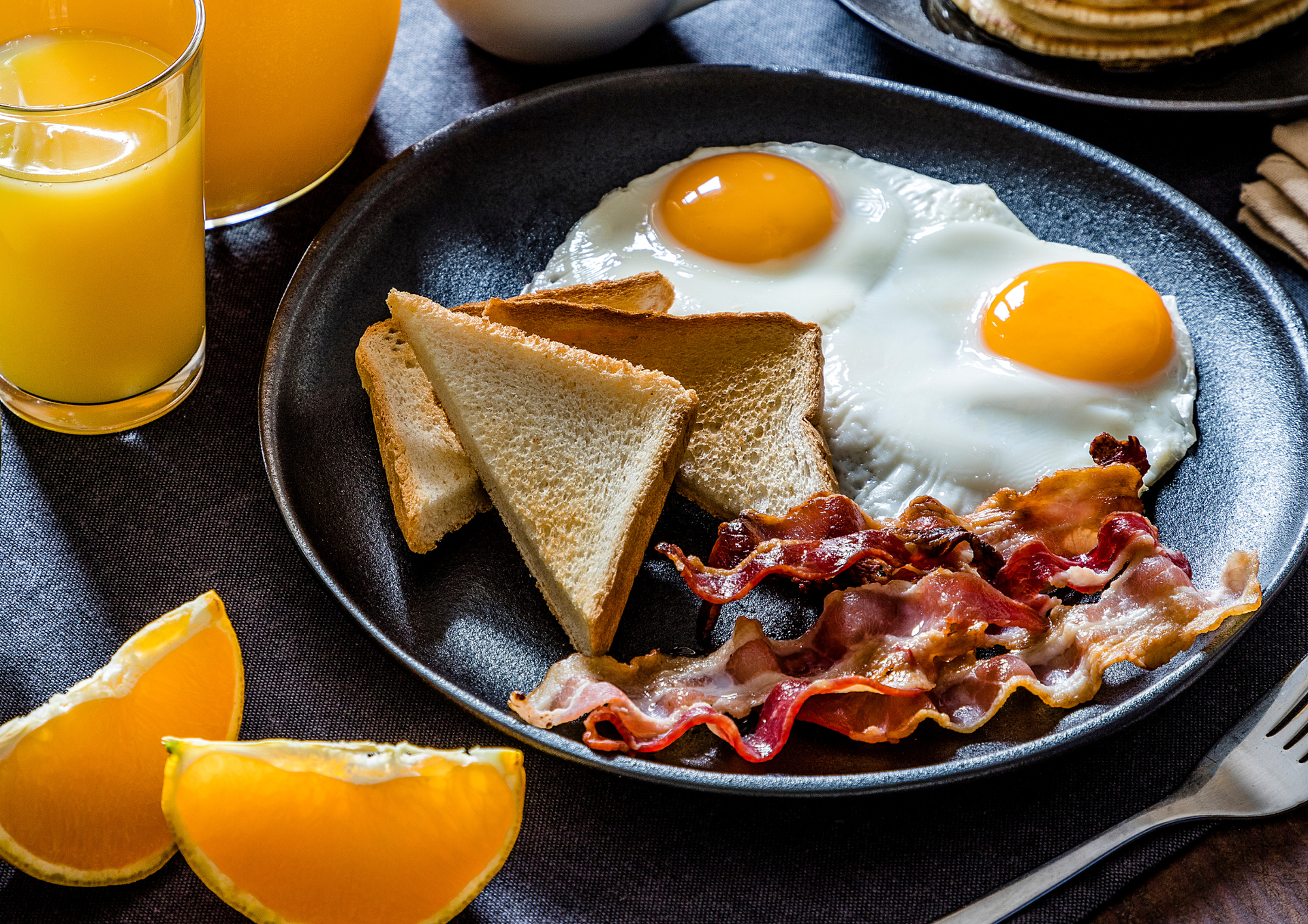 Foto di un piatto con bacon, uova e pane tostato accompagnato da un bicchiere di succo di frutta all'arancia