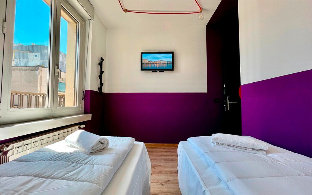 Two twin beds in a room with purple wall accent, a window, and a mounted TV.