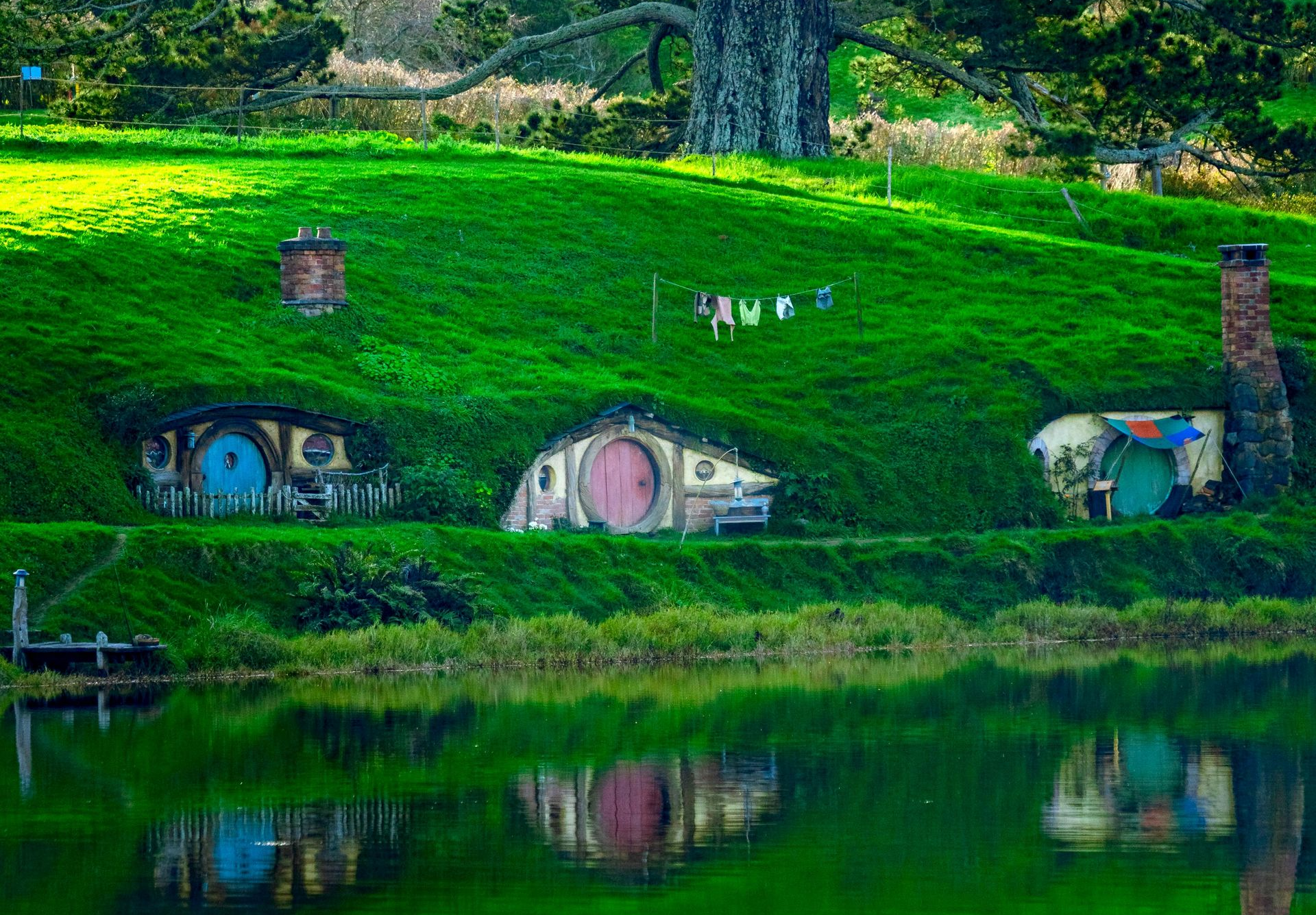 Paesaggio della Nuova Zelanda con colline verdi, un lago e le caratteristiche casette degli hobbit del Signore degli Anelli.