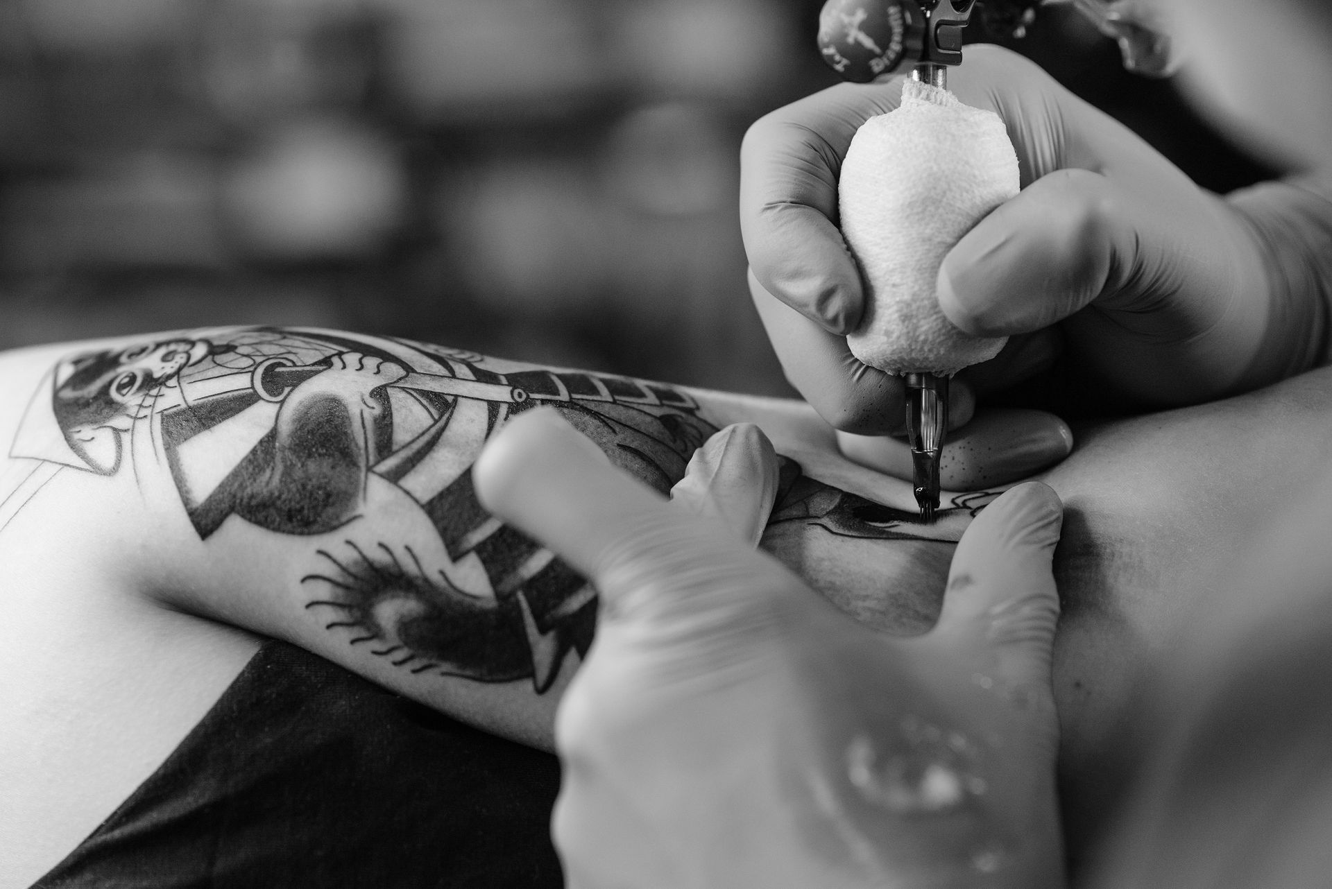 Foto in bianco e nero della mano di un tatuatore che sta tatuando un disegno su un braccio di una persona
