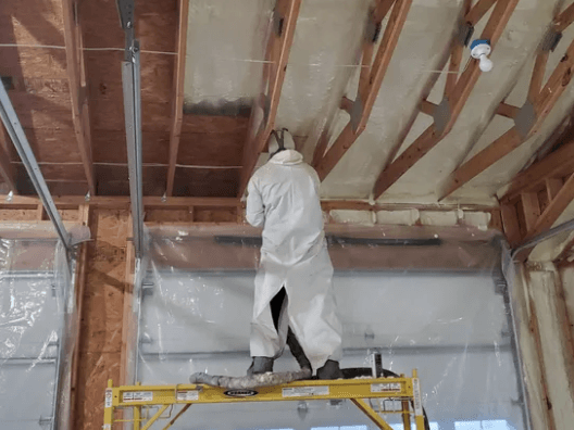 A man is spraying foam on the ceiling of a garage.