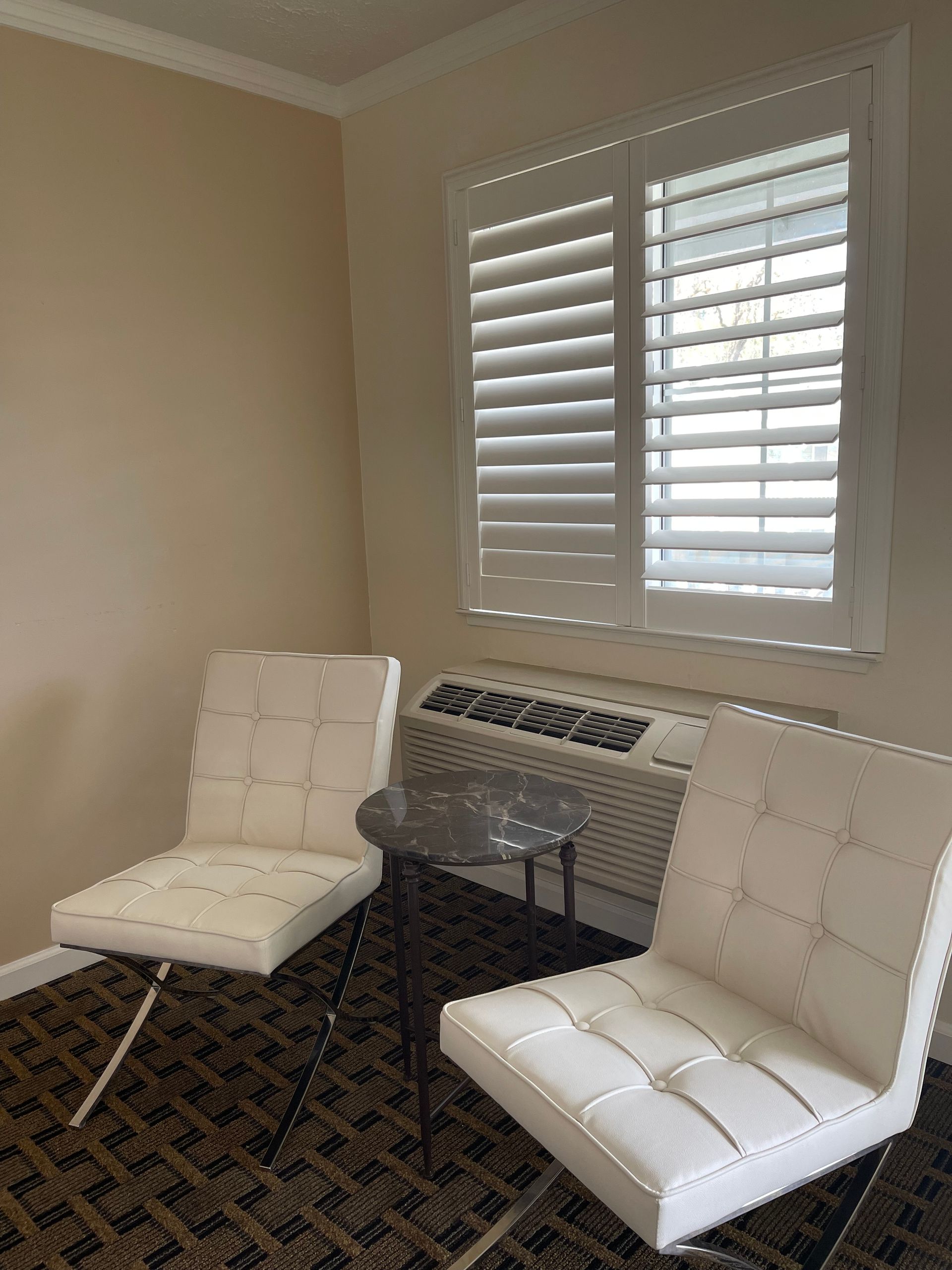 Two white chairs with a small table in front of a window with white shutters.