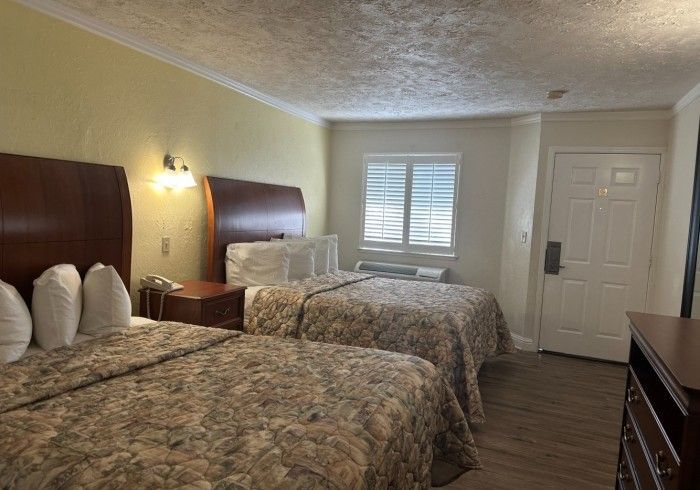 Hotel room with two double beds, window, and door. The walls are light yellow, and the beds have floral patterned comforters.