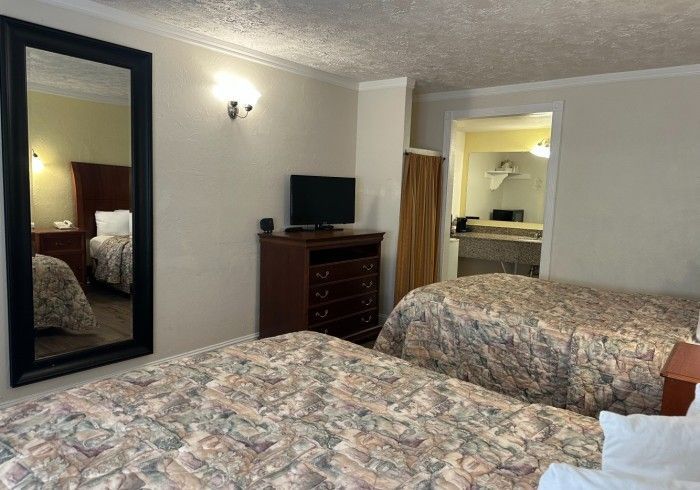 Hotel room with two beds, dresser with TV, mirror reflecting bed, and open bathroom.