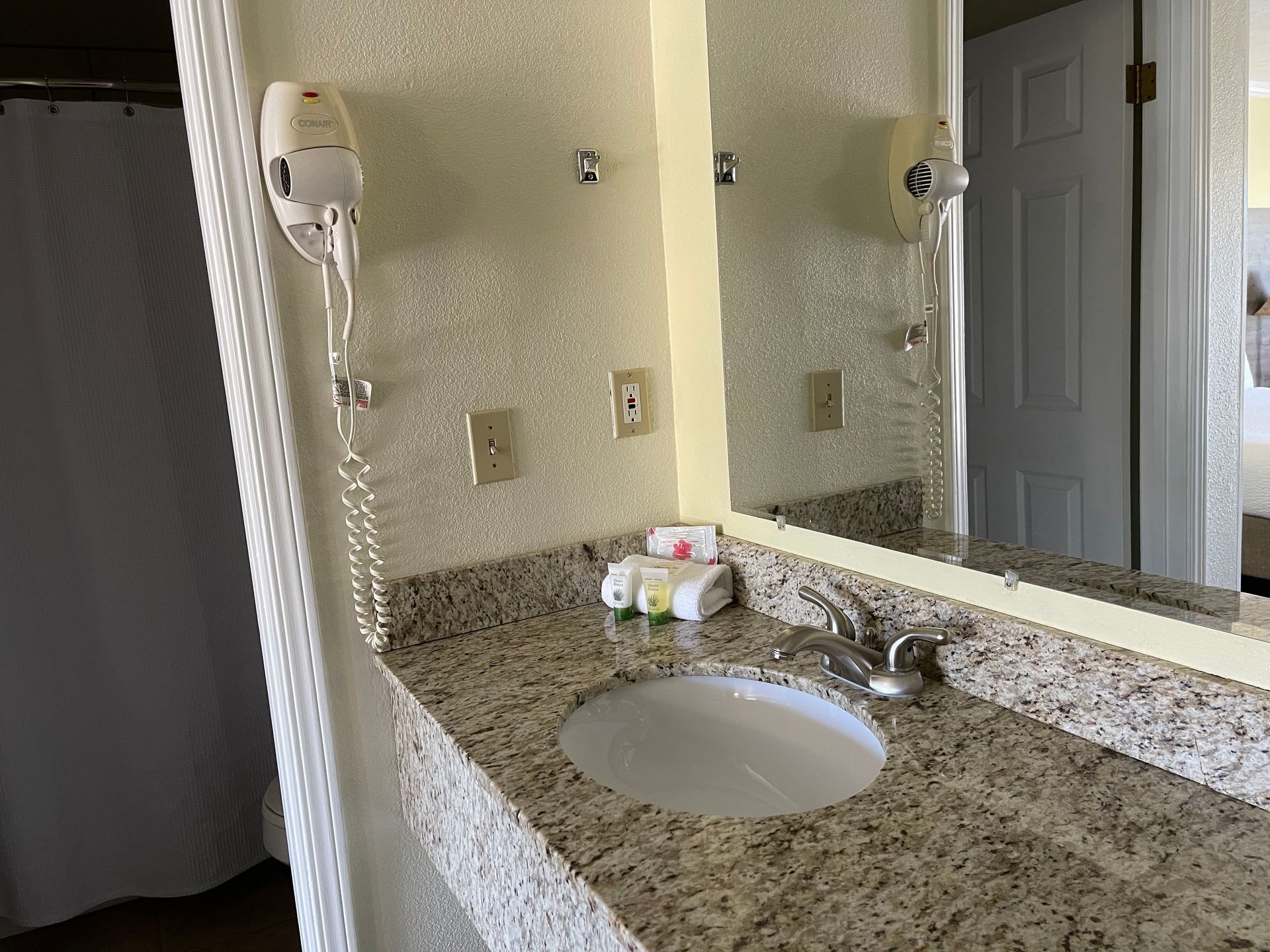 Bathroom vanity with mirror, sink, hairdryer, and toiletries.