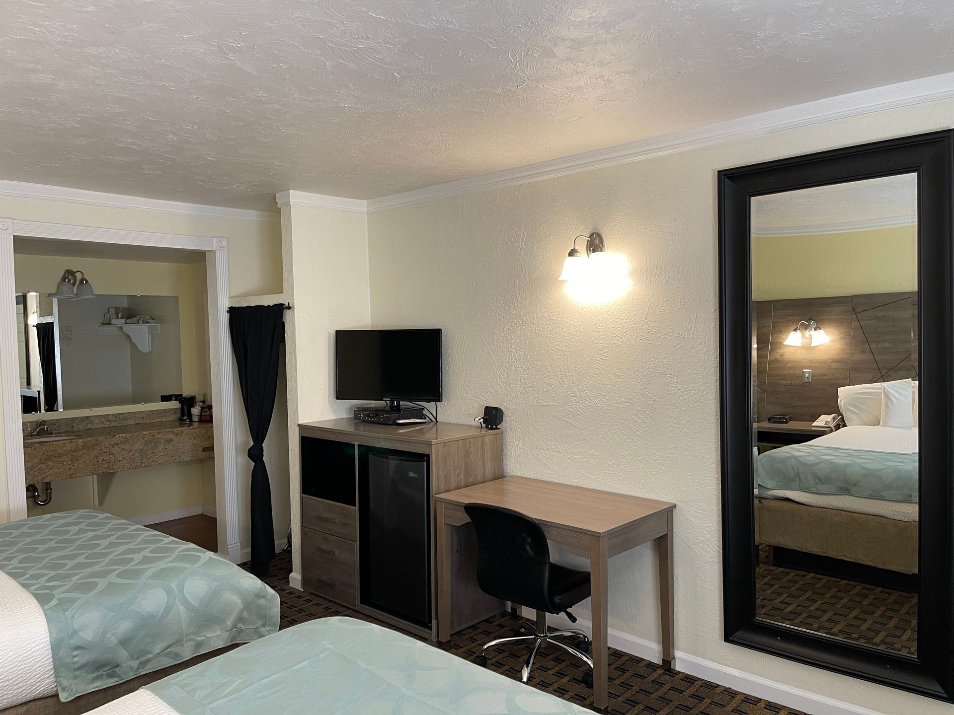 Hotel room with two beds, desk, mirror, and a bathroom visible.