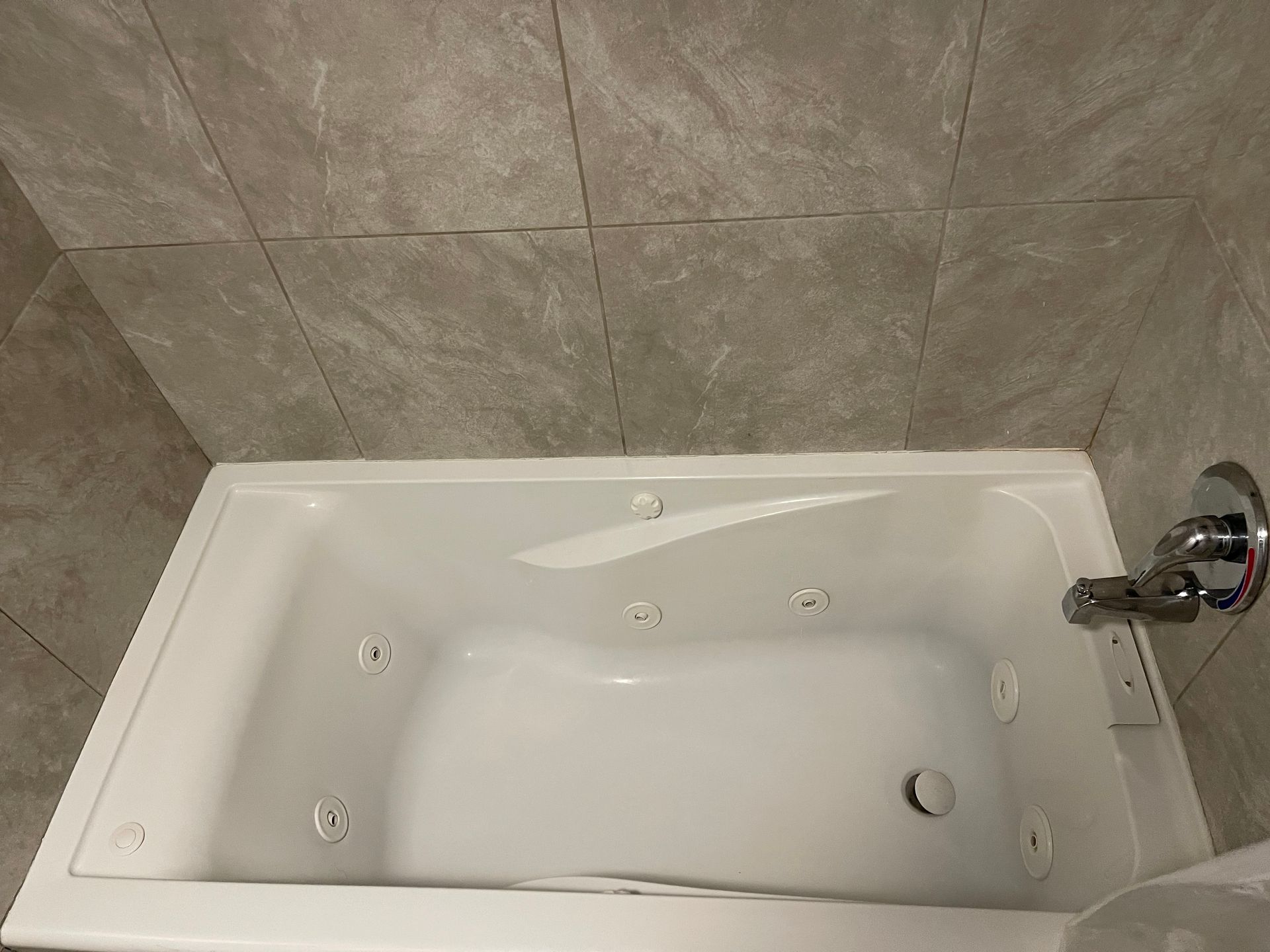 White bathtub with jets, faucet, set against gray tiled wall.