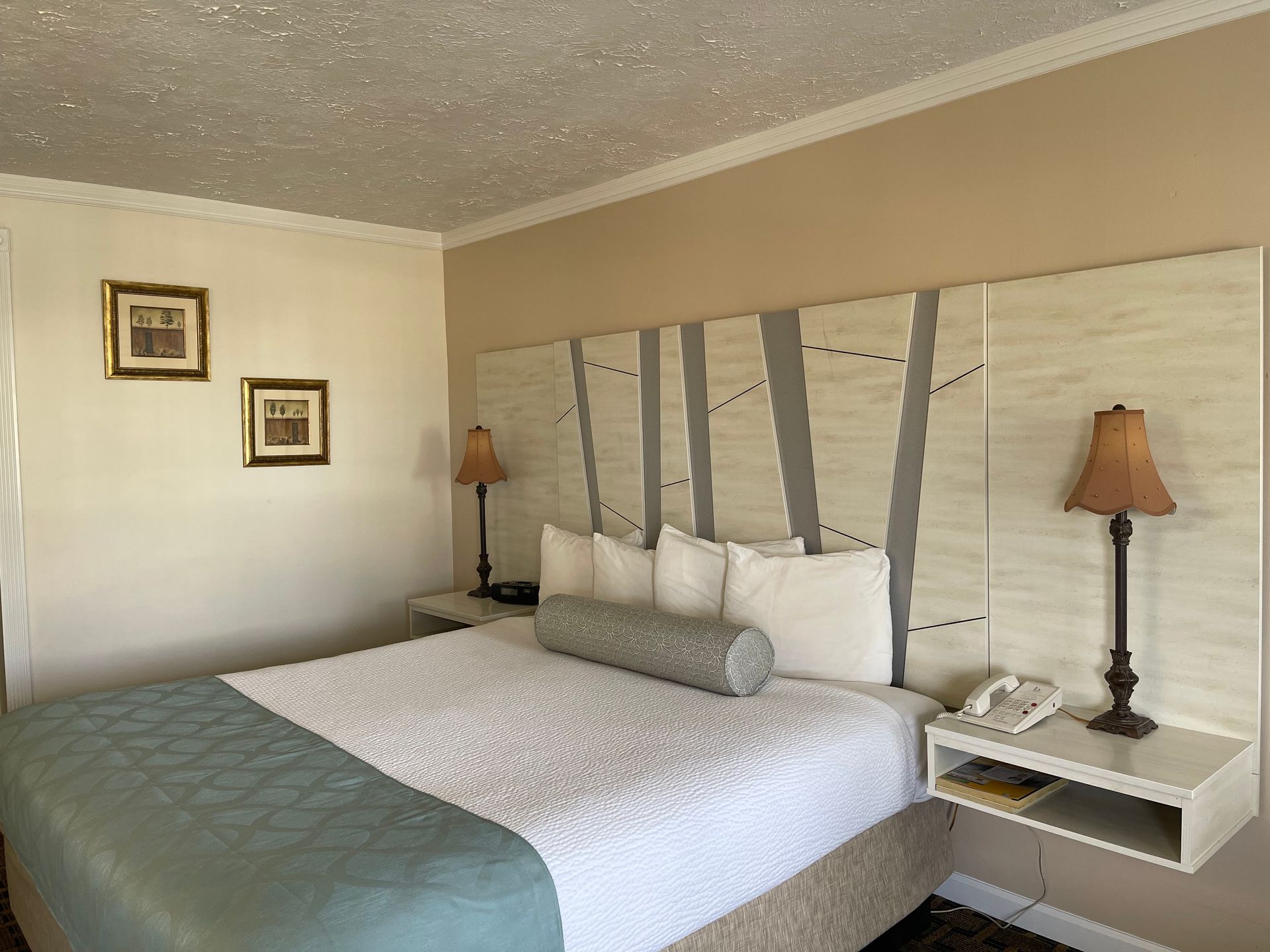 Bedroom with a bed, nightstands, lamps, artwork, and a patterned headboard. Beige and white tones.