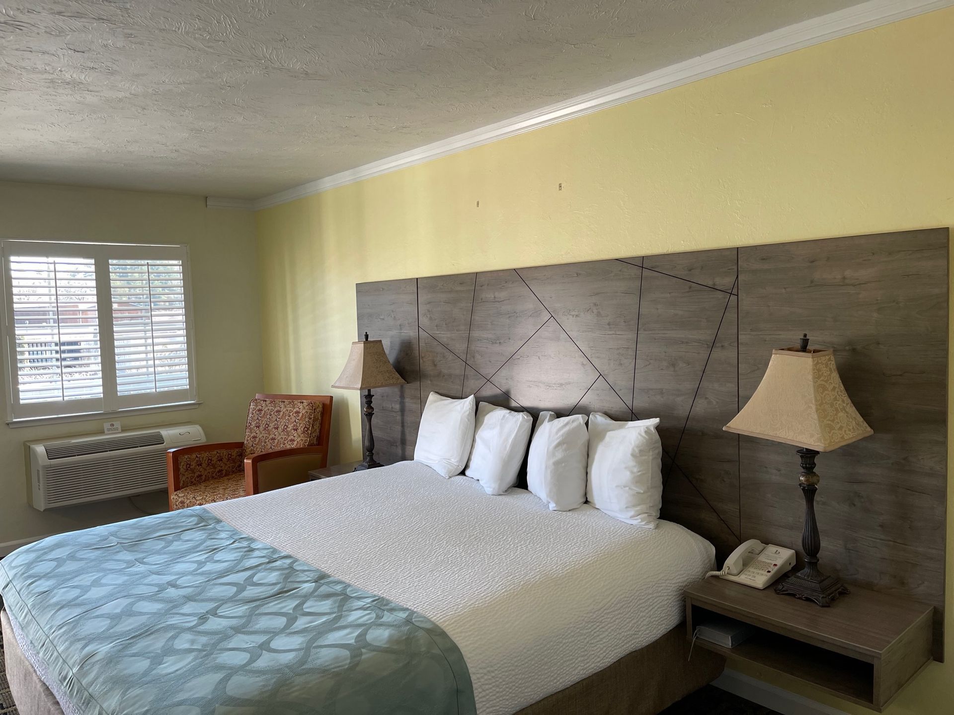 Bedroom with a large bed, nightstand, lamps, and a window with blinds.