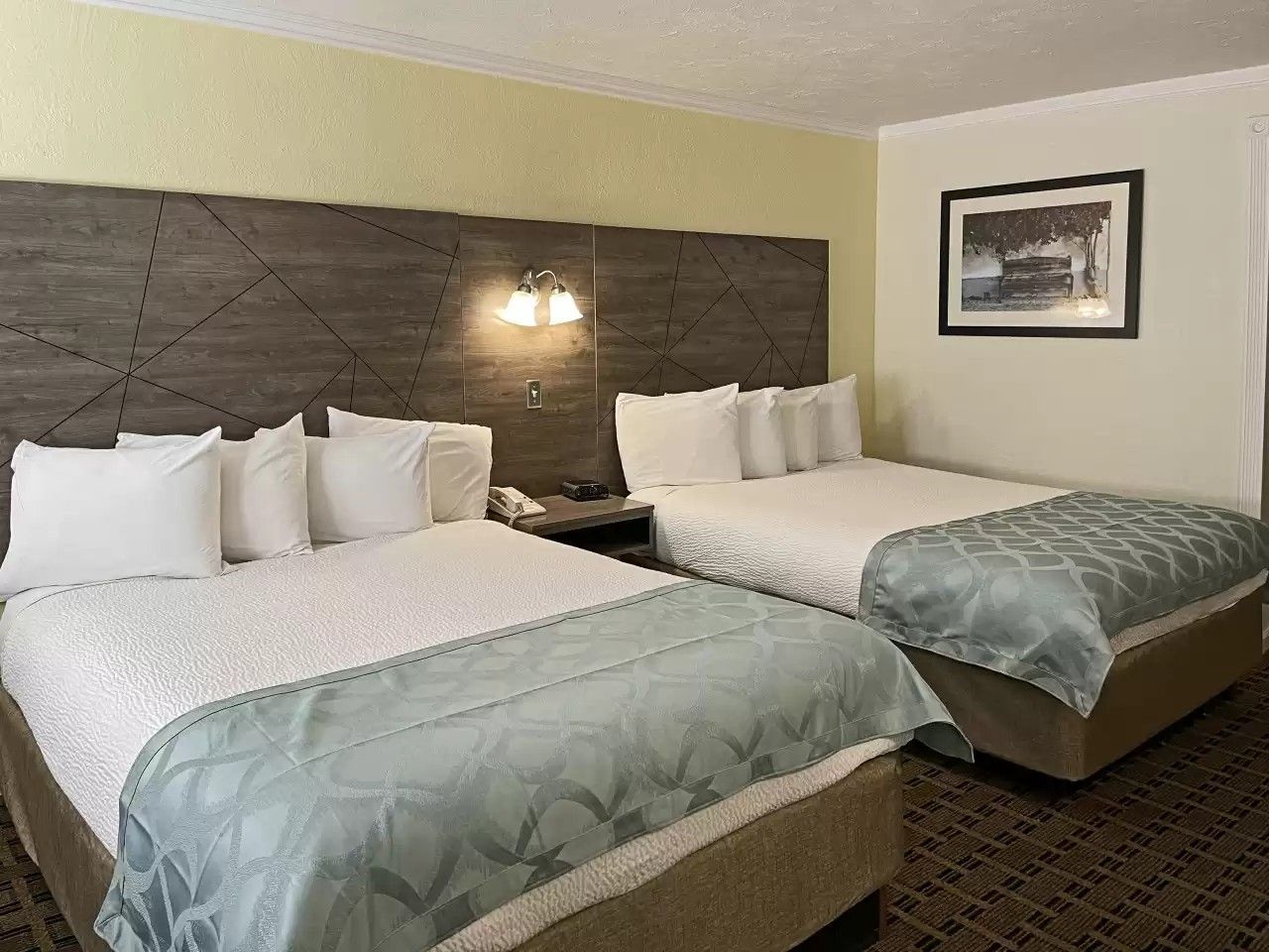Two double beds in a hotel room, light blue comforters, a picture on the wall.