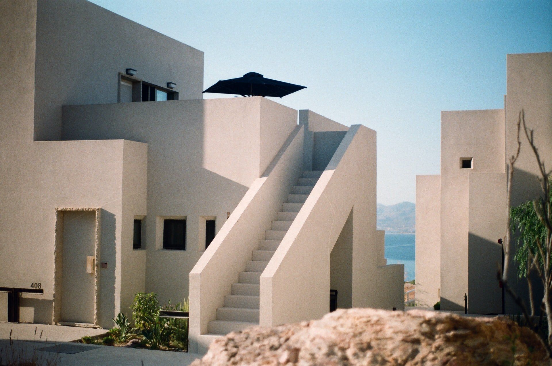 White architectural complex with staircases, an open door, and ocean view.