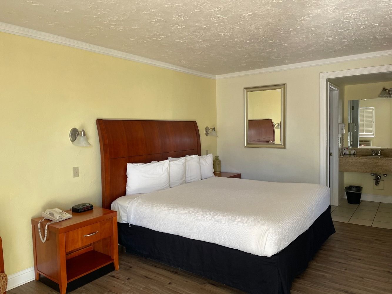Bedroom with a king-size bed, nightstand, mirror, and bathroom door. The walls are yellow.