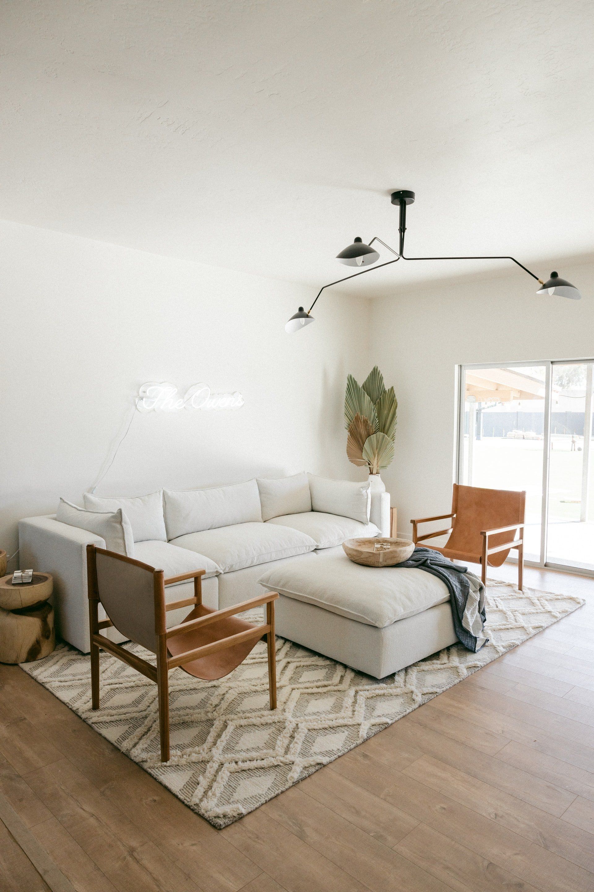 Living room with white sectional, two leather chairs, patterned rug, and a modern light fixture.