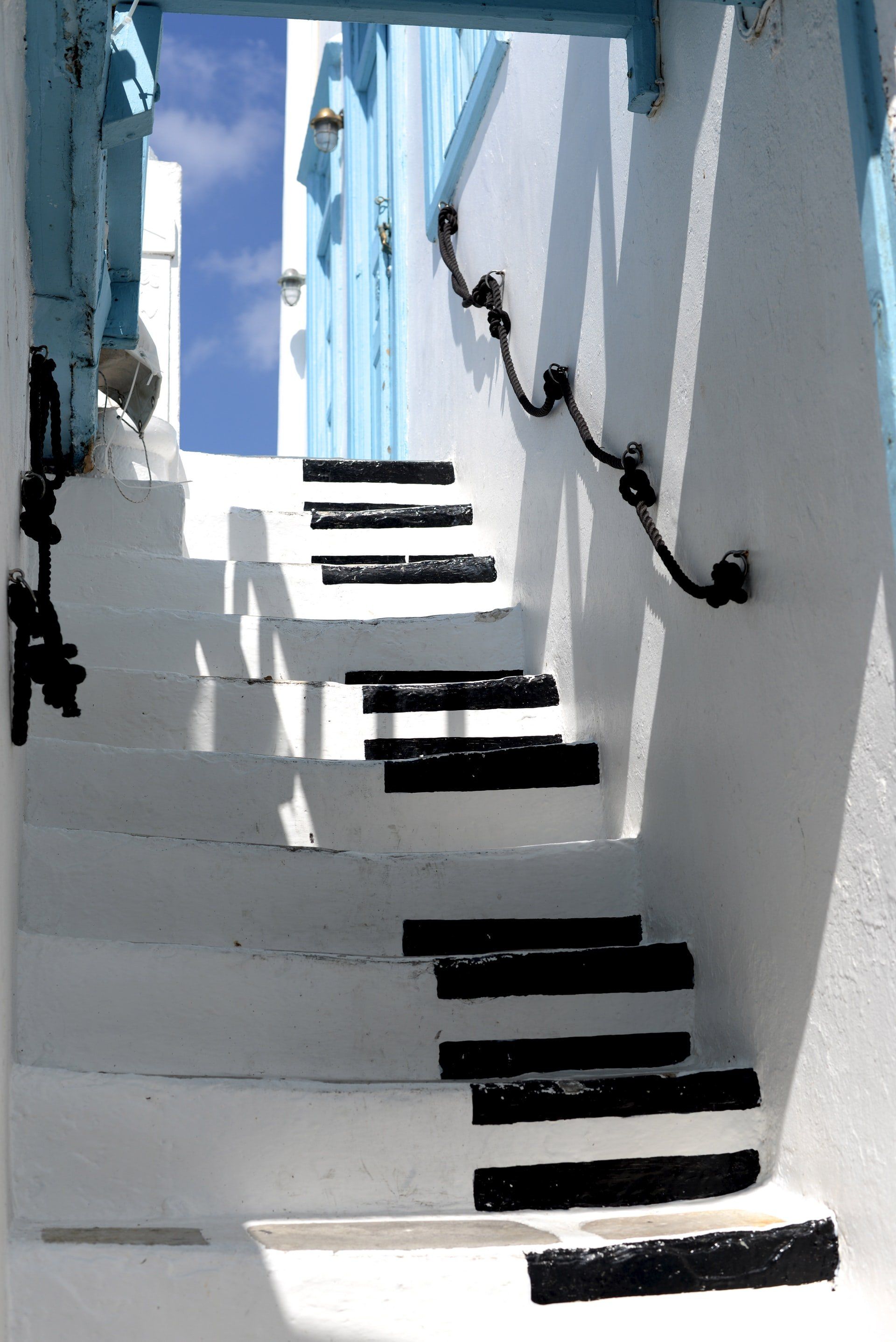 White stairs with black steps against white wall, blue accents, sunny sky.