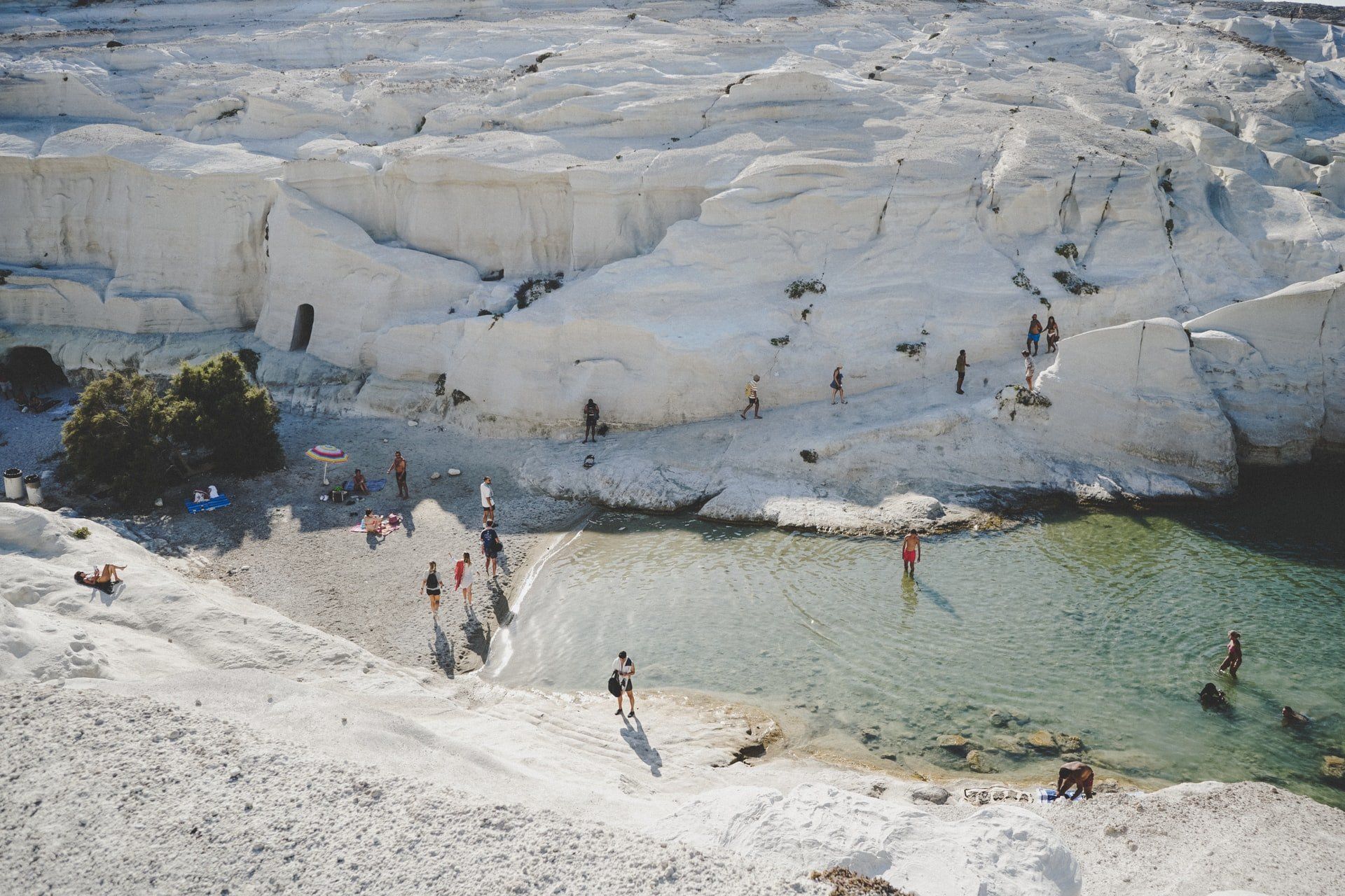 White cliffs overlook a shallow, clear-water cove with people swimming and relaxing on the beach.