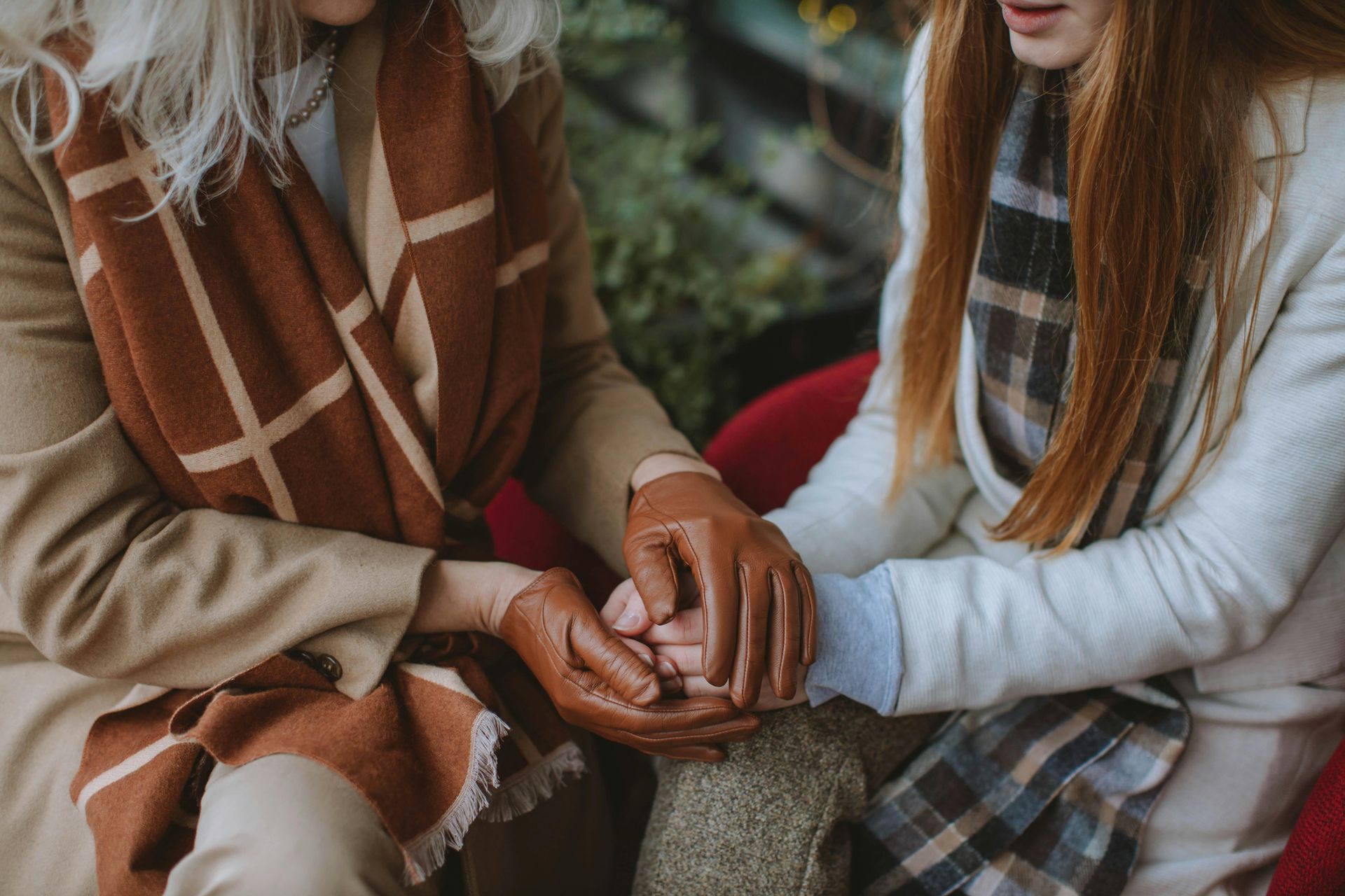 Two women holding hands, one wearing gloves and a brown scarf.