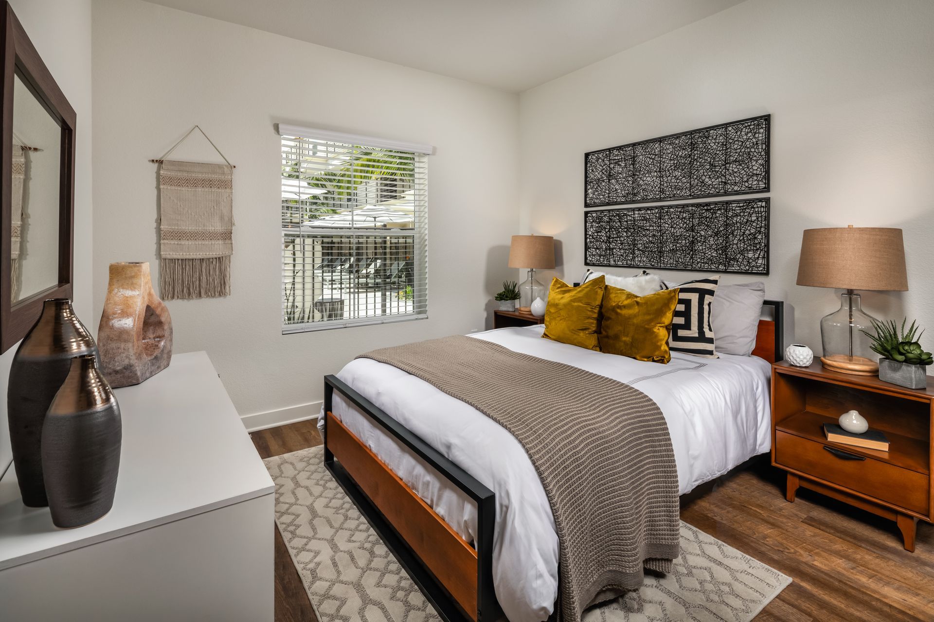 A bedroom with a bed , dresser , nightstand , mirror and window.