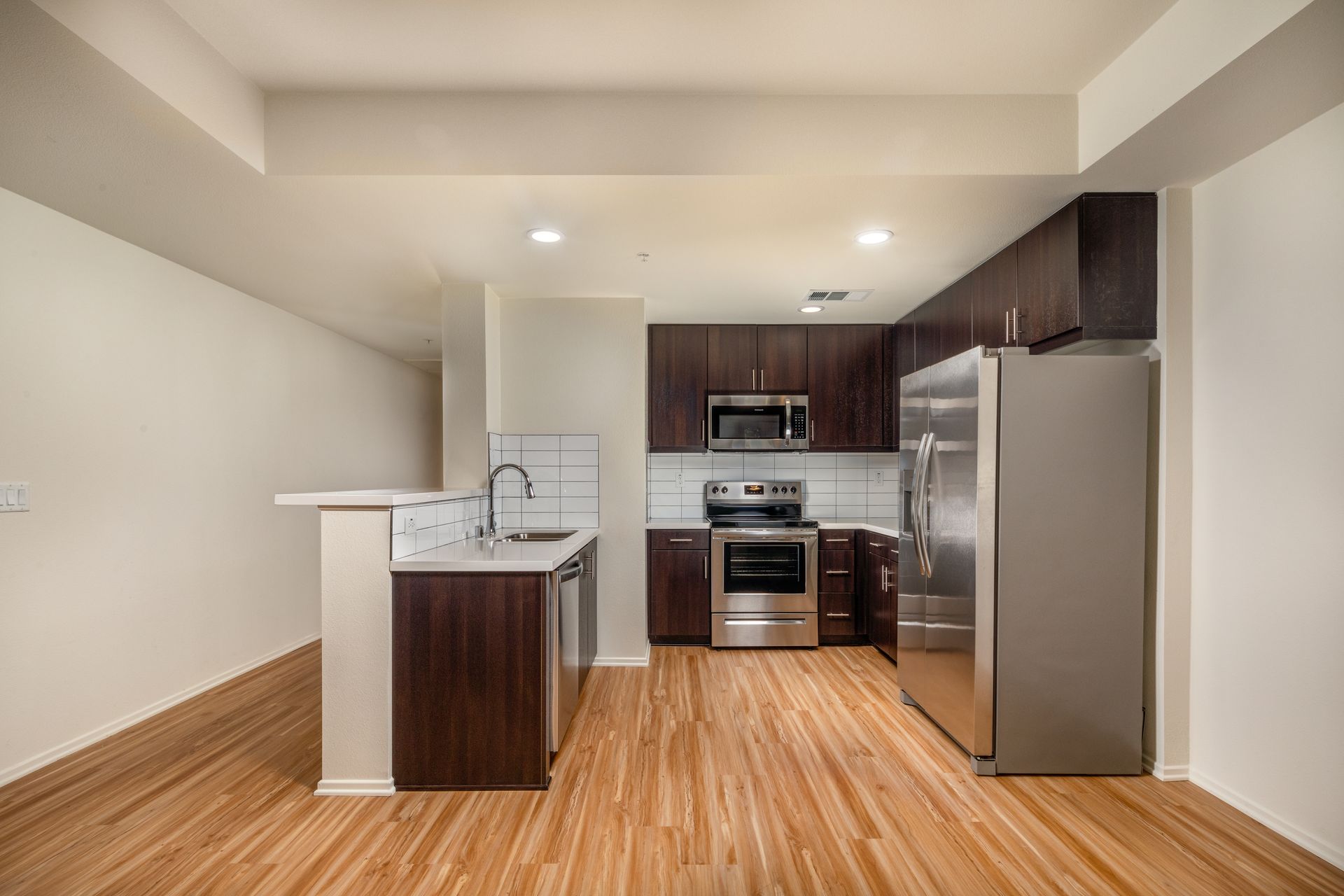 An empty kitchen with wooden floors and stainless steel appliances.