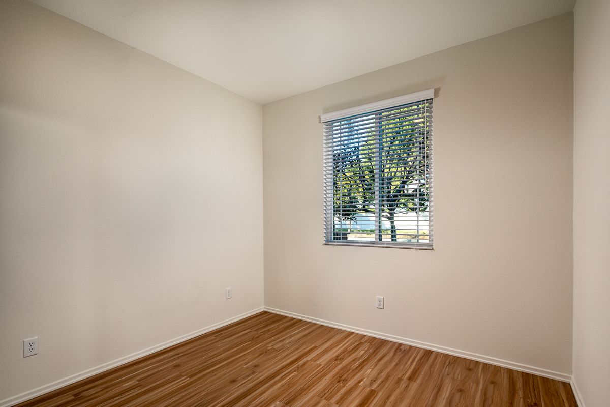 An empty bedroom with hardwood floors and a window with blinds.