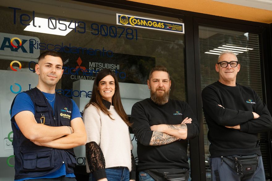 Quattro persone in posa davanti alla vetrina di un'attività commerciale. Sorridono e tengono le braccia incrociate.