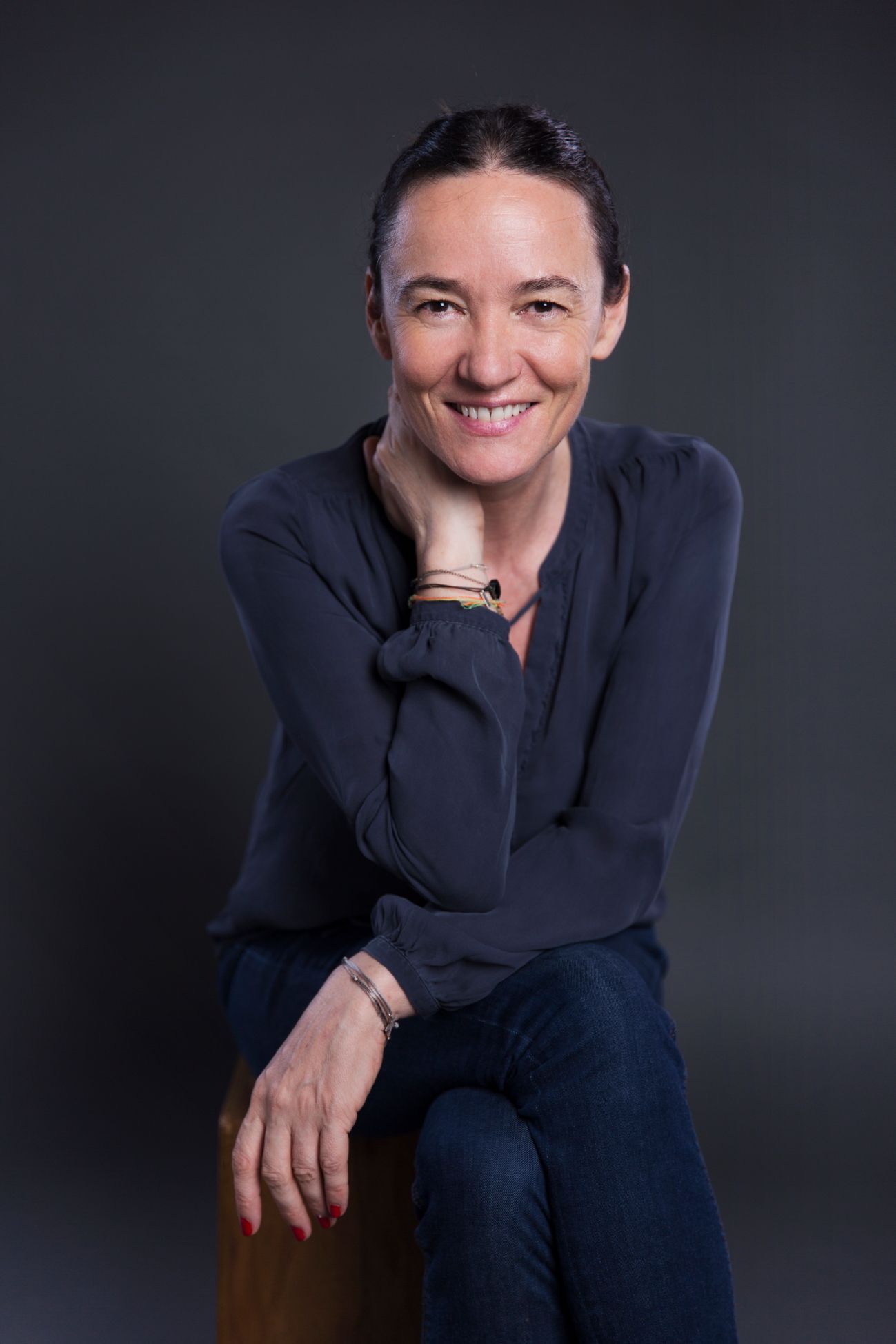 Une personne souriante, le menton appuyé sur la main, vêtue d'une chemise sombre à manches longues et d'un jean