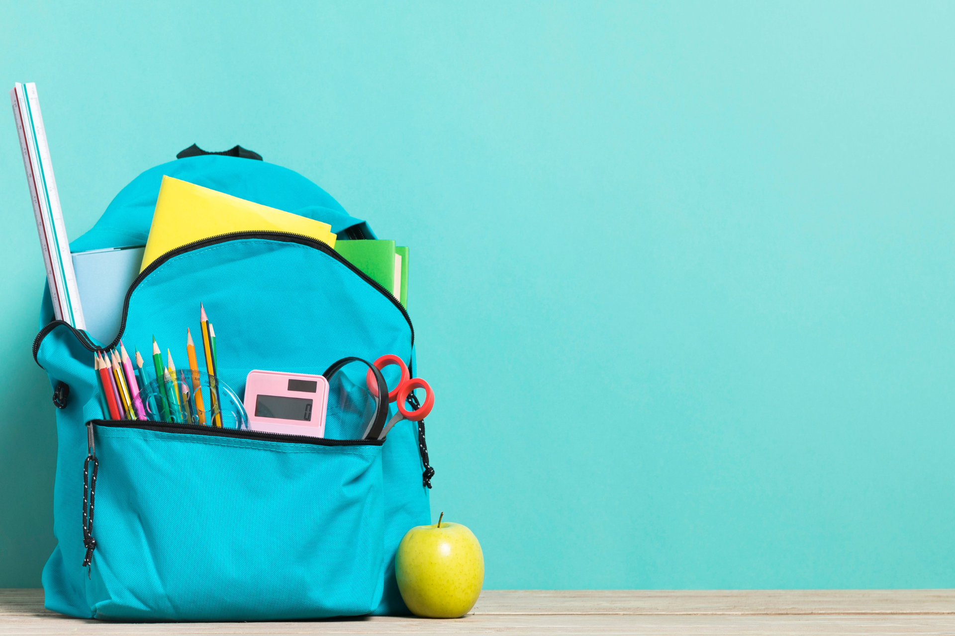 A blue backpack filled with school supplies and an apple on a table.
