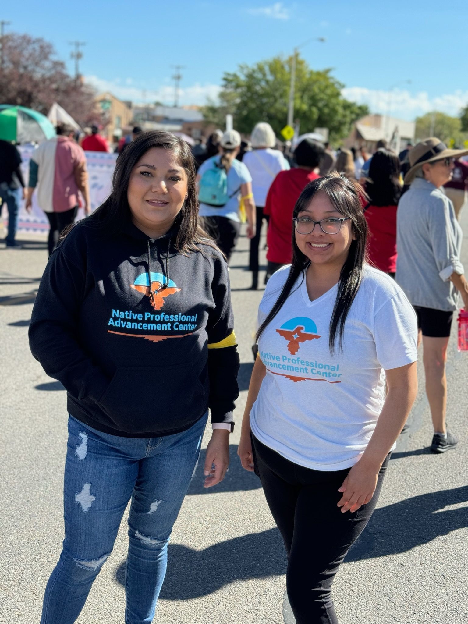 Two women are standing next to each other in front of a crowd at a protest.