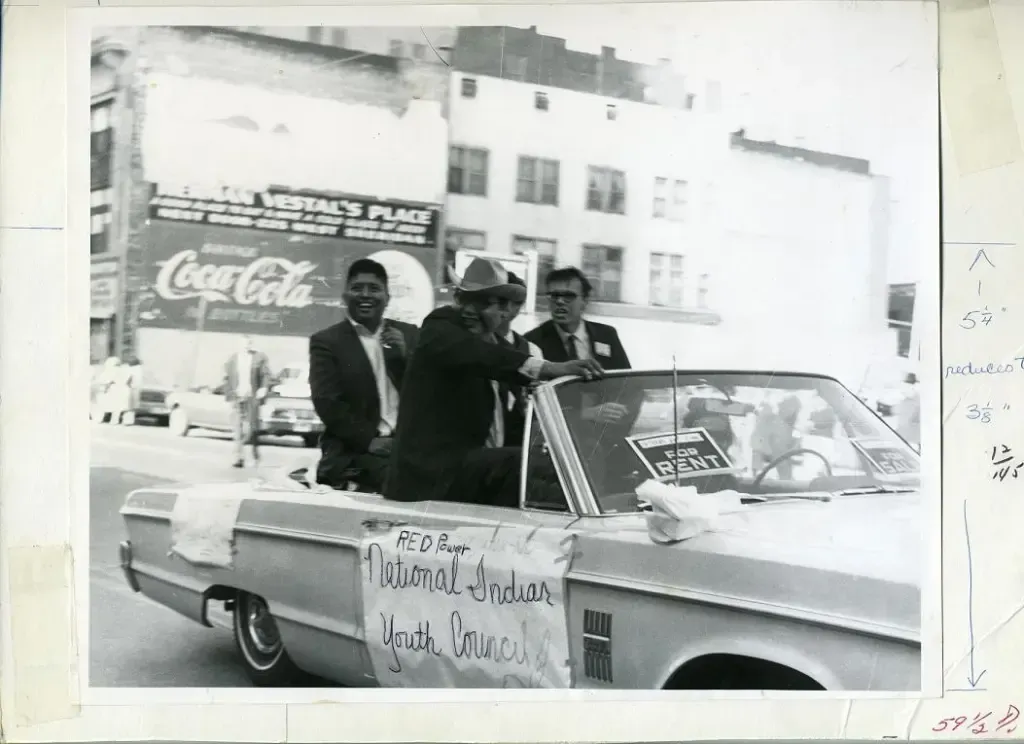 A black and white photo of men in a car with a coca cola sign in the background