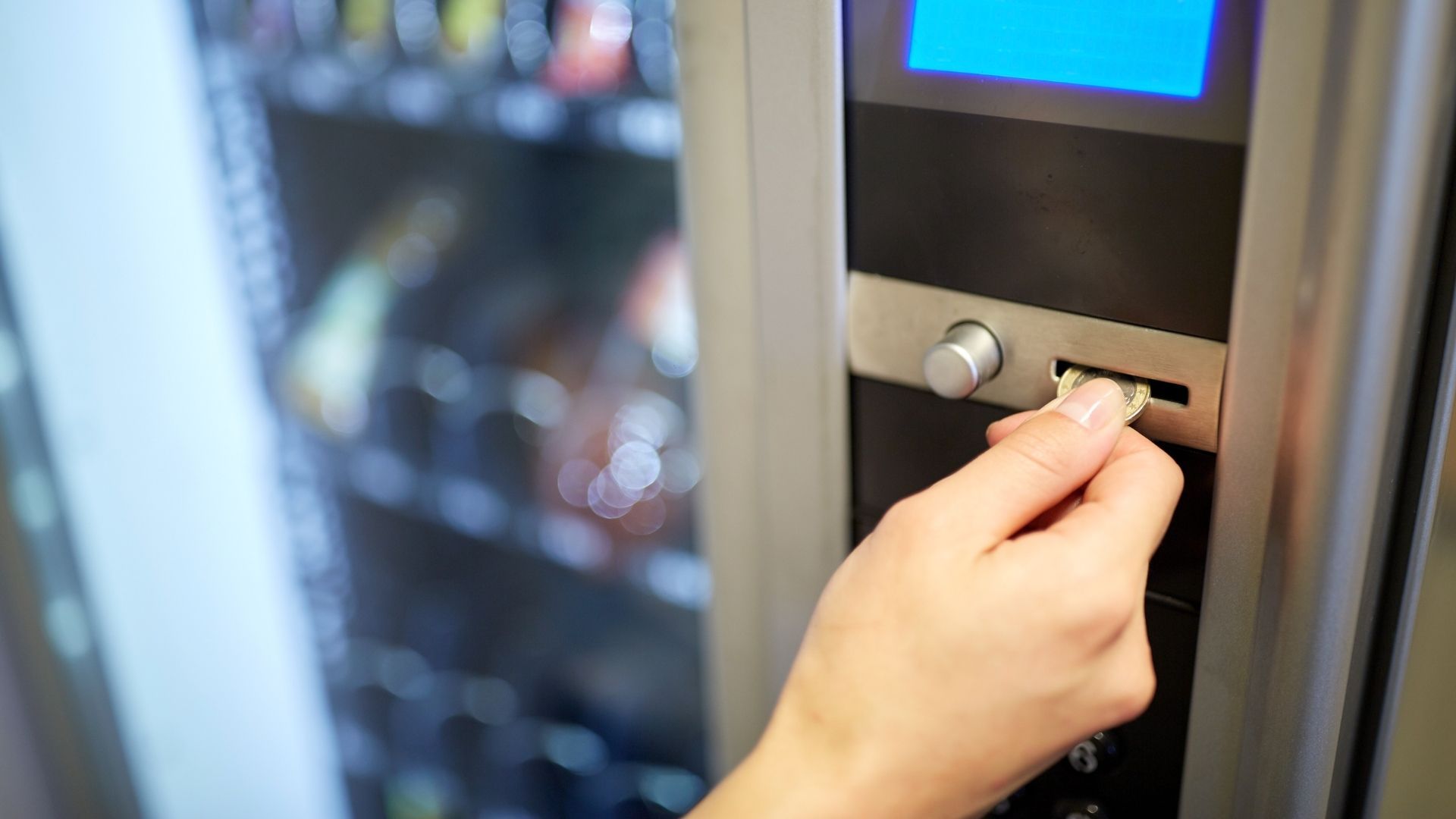 Hand inserting a bill into a vending machine to purchase a snack or drink.