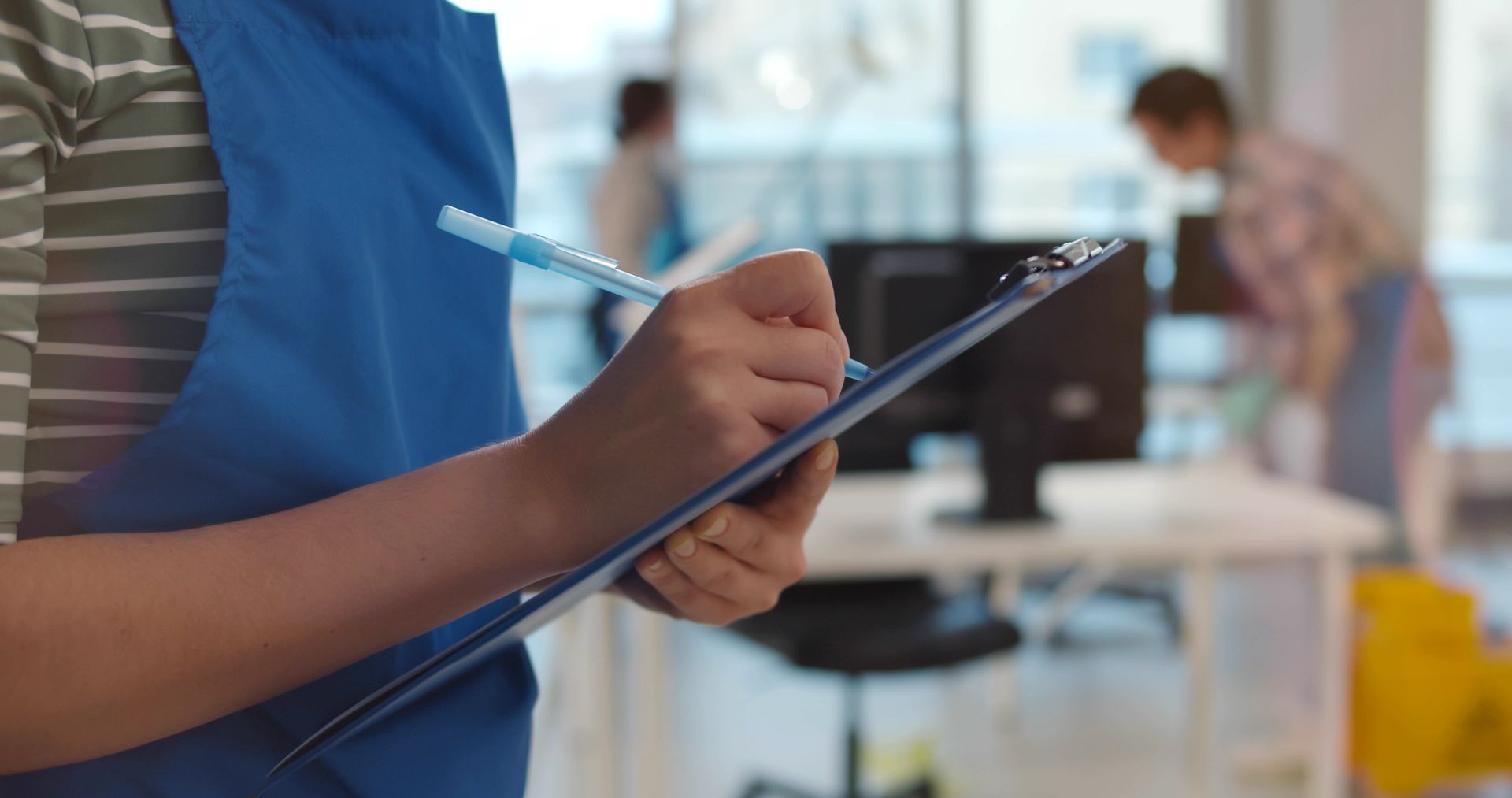 Three people cleaning a bright living room: wiping furniture, adjusting pillows, rolling up a rug.