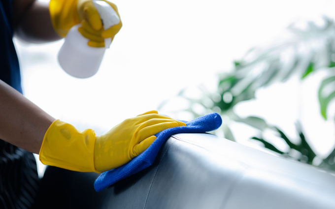 Woman in gloves cleaning a table with a spray bottle near a potted plant.