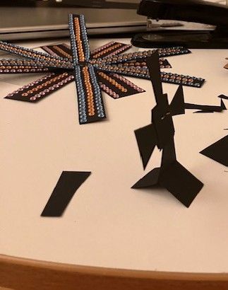 Abstract black paper sculptures on a white table, with a colorful radial design in the background.