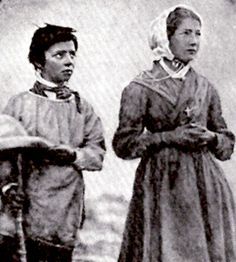 Two people in old-fashioned clothing stand side by side with folded arms in a black-and-white photo