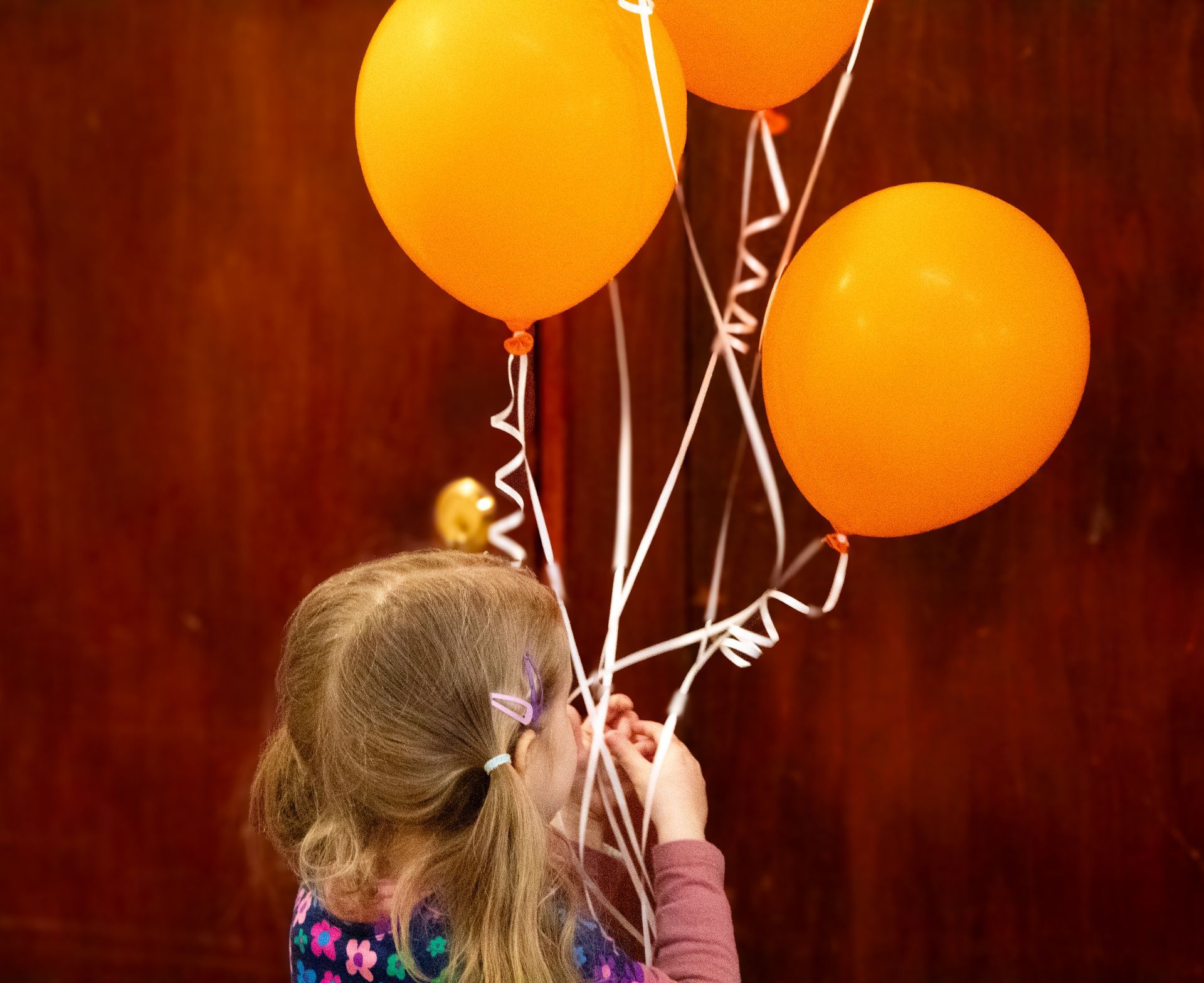 A little girl is holding a bunch of orange balloons