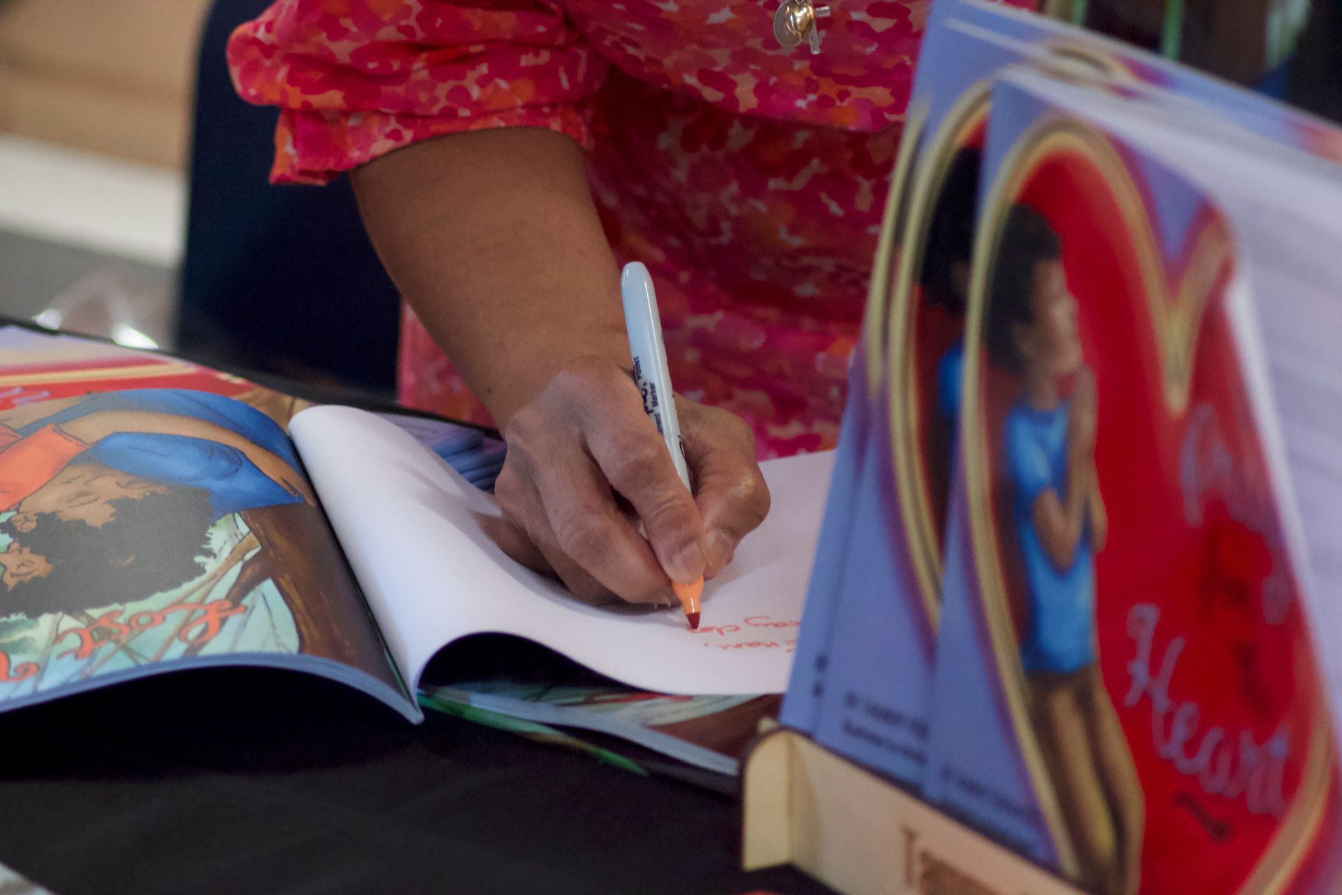 A person is writing on a piece of paper next to a book that says heart