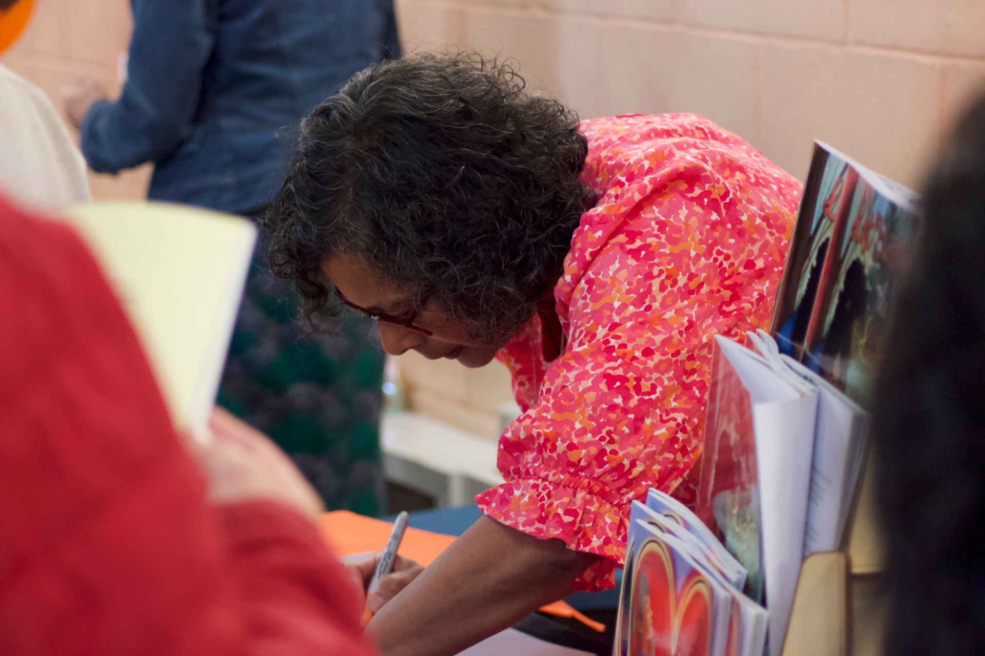 A woman in a red shirt is writing on a piece of paper.