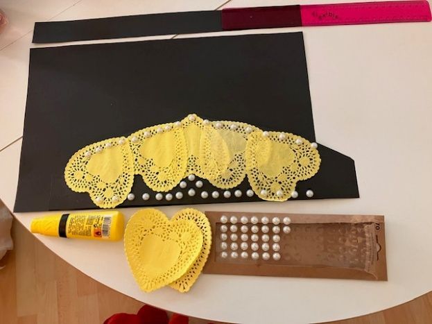 Yellow paper doily crafts arranged on black and brown cardstock with glue sticks and pearl dots